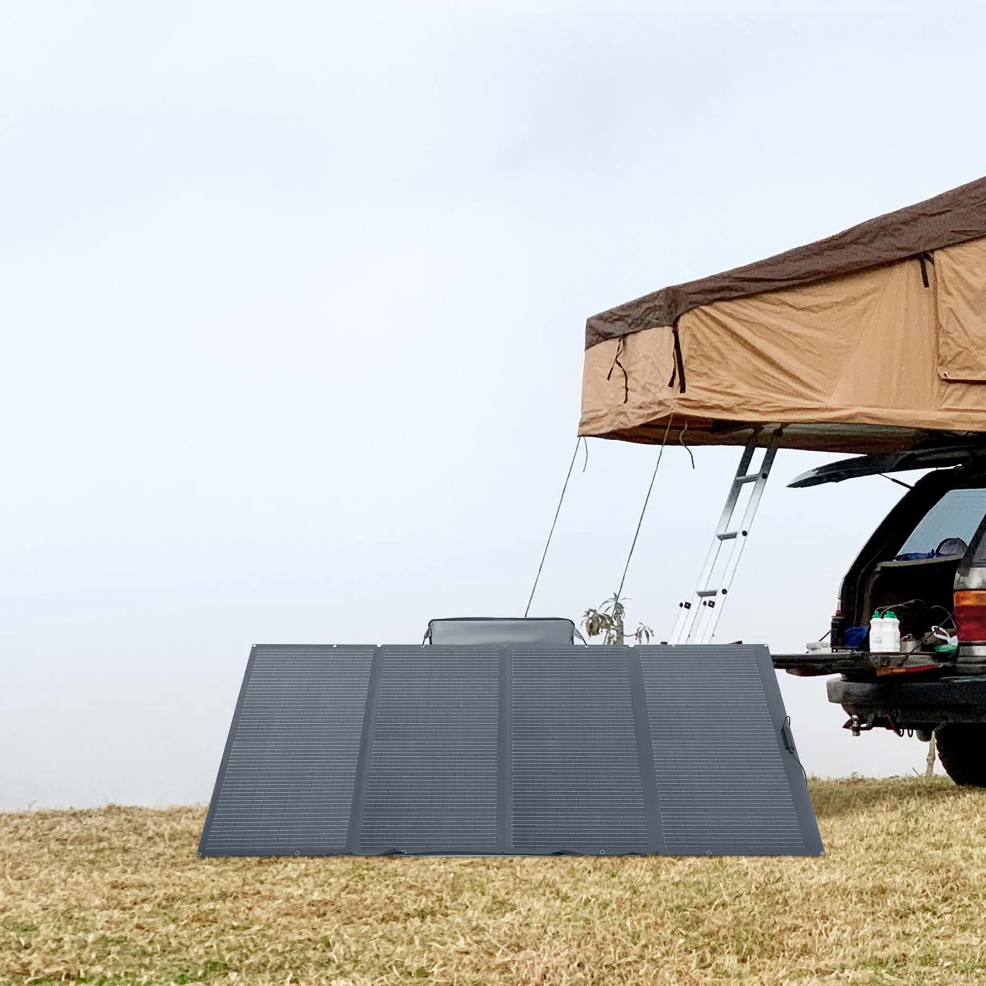 Faltbares dunkelgraues 400-Wp-Solarmodul mit mehreren Panelen steht auf einer Wiese vor einem Fahrzeug mit Dachzelt
