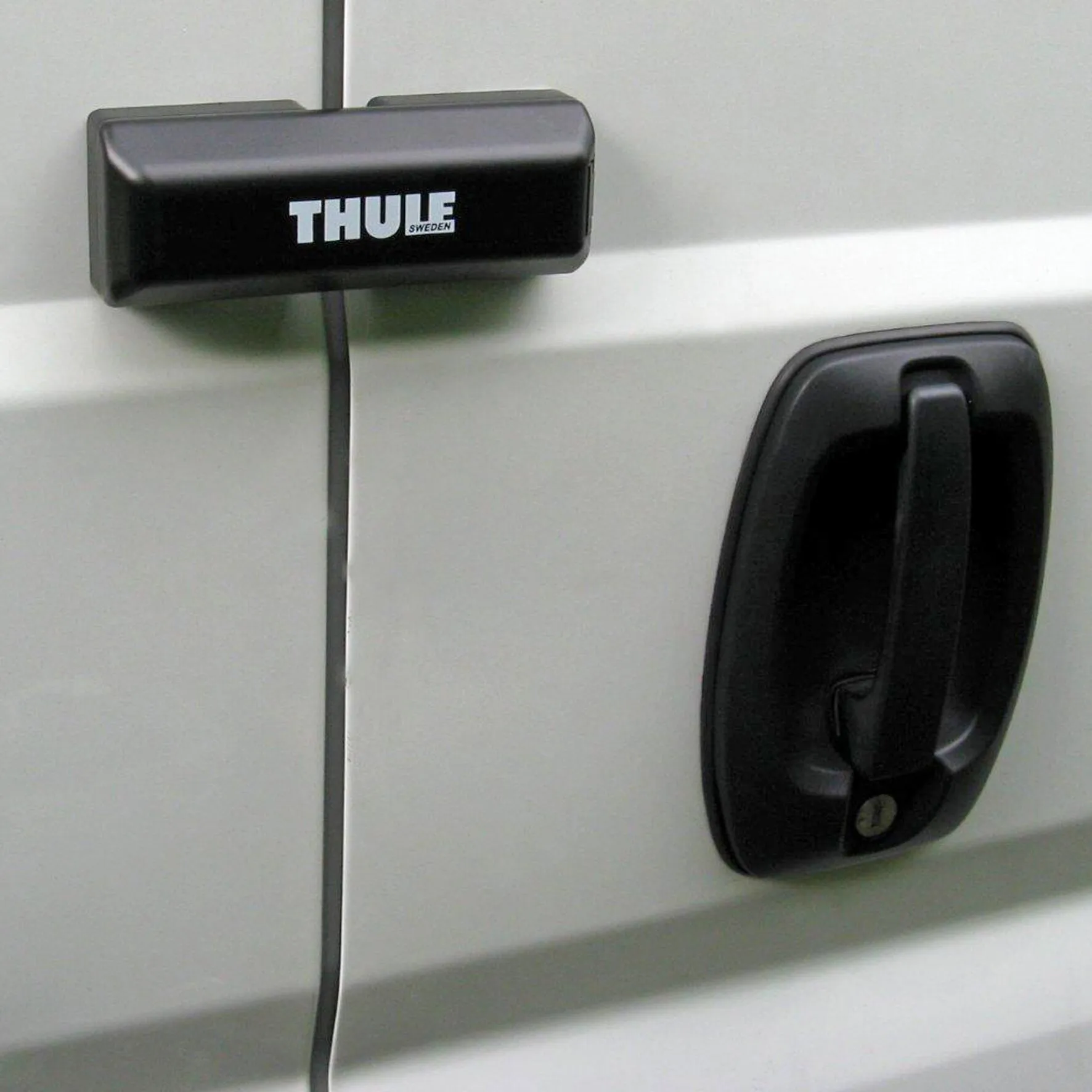 Schwarze THULE Van-Lock-Türverriegelung an den Hecktüren eines weißen Transporters mit sichtbarem Schließzylinder
