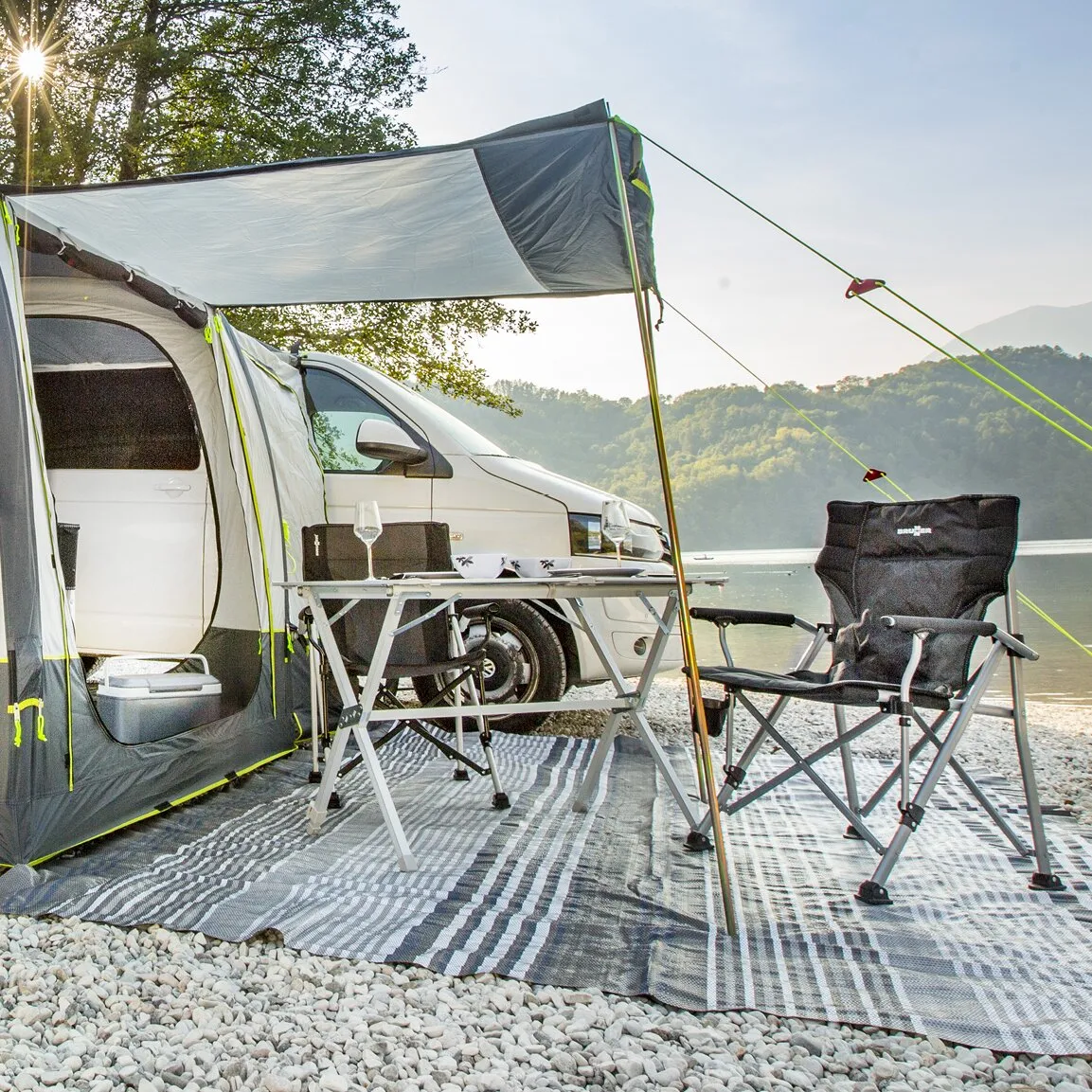 Schwarzer Faltstuhl Raptor NG 2.0 mit Armlehnen vor einem Campingzelt am See neben einem Campingtisch