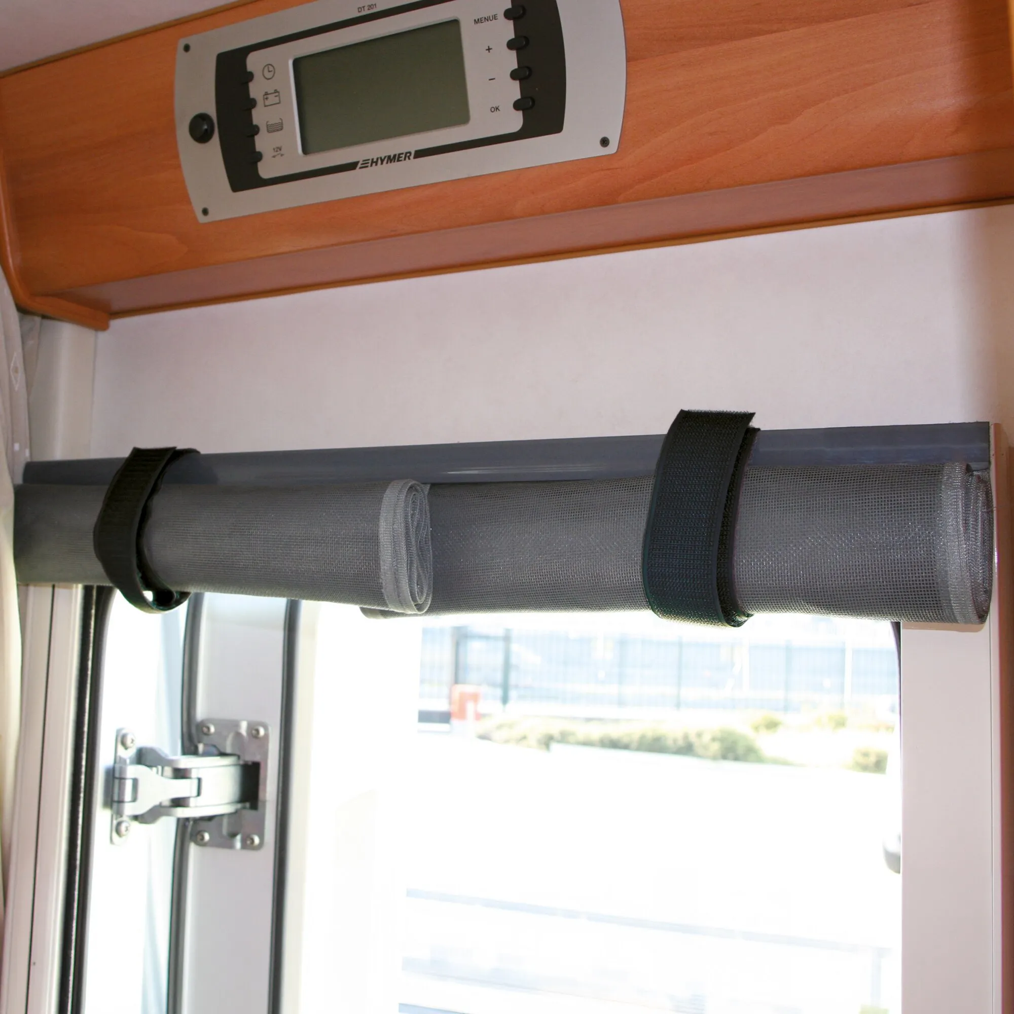 Aufgerolltes graues Moskitonetz als Türvorhang mit schwarzen Befestigungsriemen über der geöffneten Wohnmobiltür