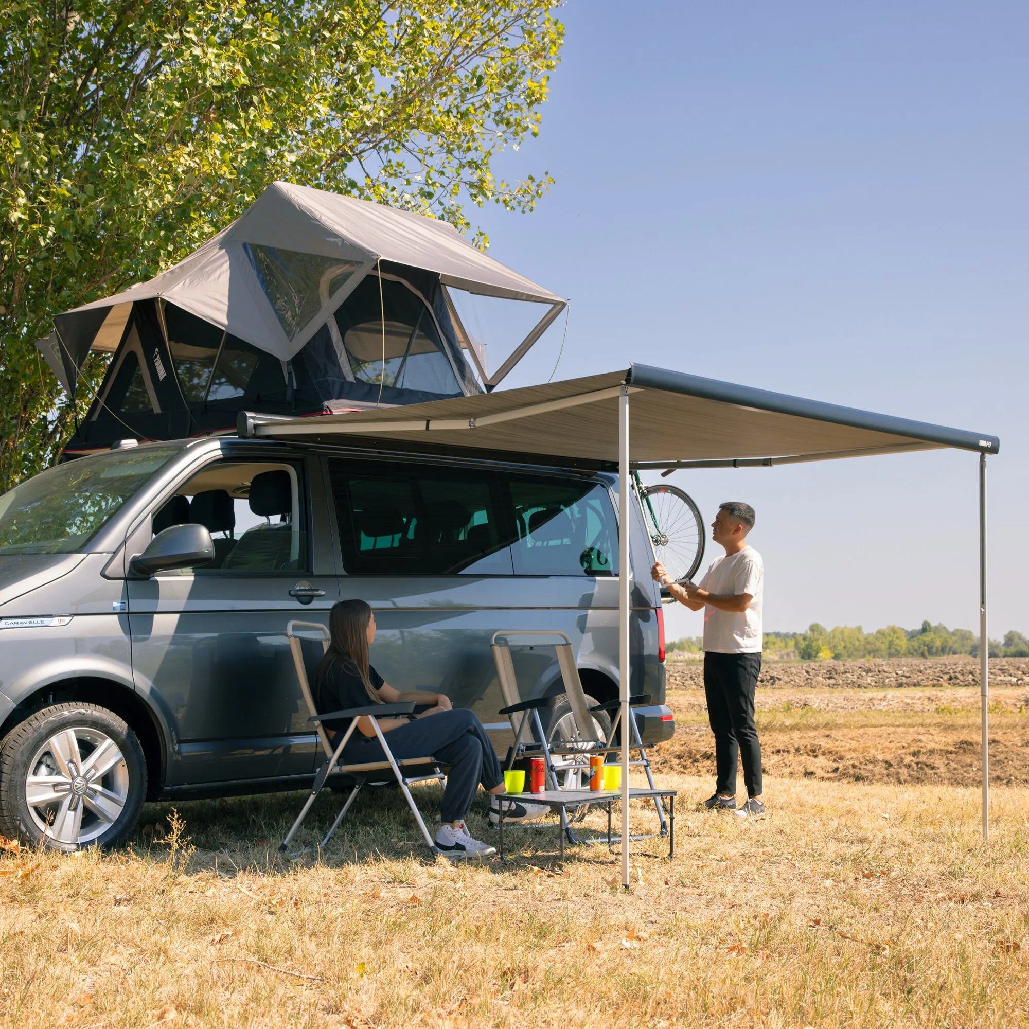 Ausgefahrene Markise F43van, 300 cm, an einem Campingbus mit Dachzelt; zwei Personen nutzen den schattigen Bereich darunter