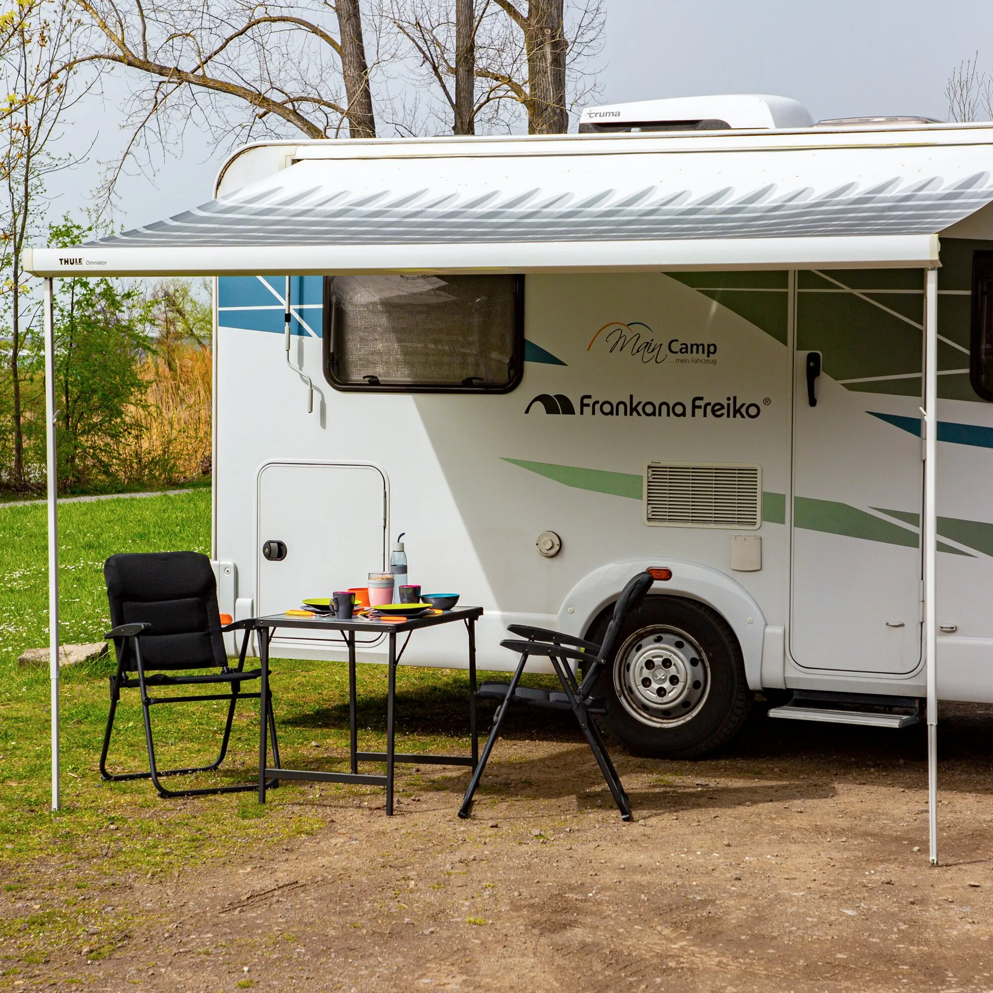 Schwarzes Compact Stuhl-/Tischset mit zwei Klappstühlen und gedecktem Campingtisch unter der Markise eines Wohnwagens