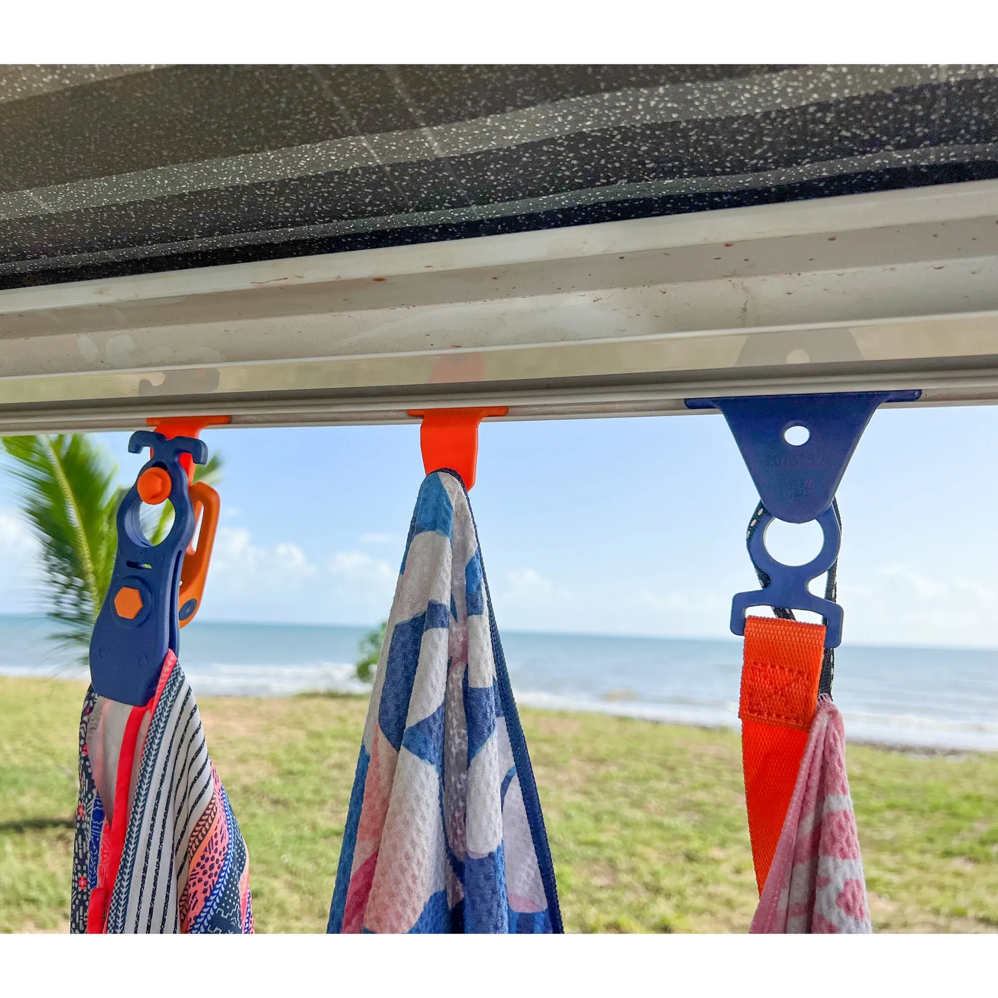 Blaue und orange PP-Croc-Adapter in einer Kederschiene befestigen Handtücher und Kleidung unter einer Markise am Strand