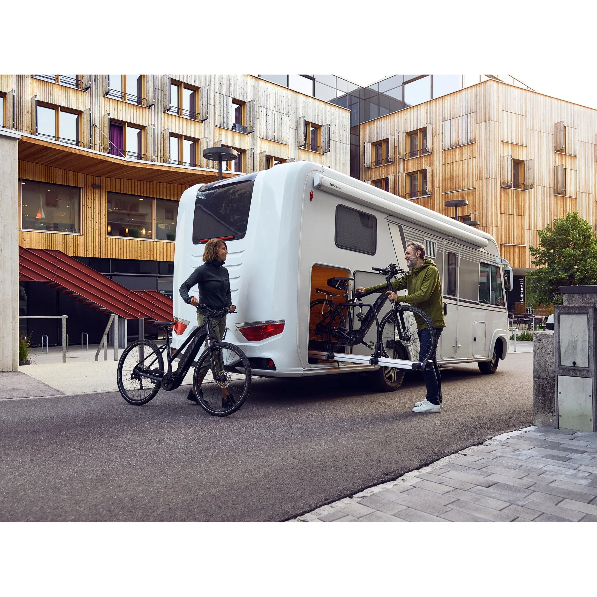 Thule VeloSlide Fahrradträger am Heck eines weißen Wohnmobils mit zwei Fahrrädern und zwei Personen davor