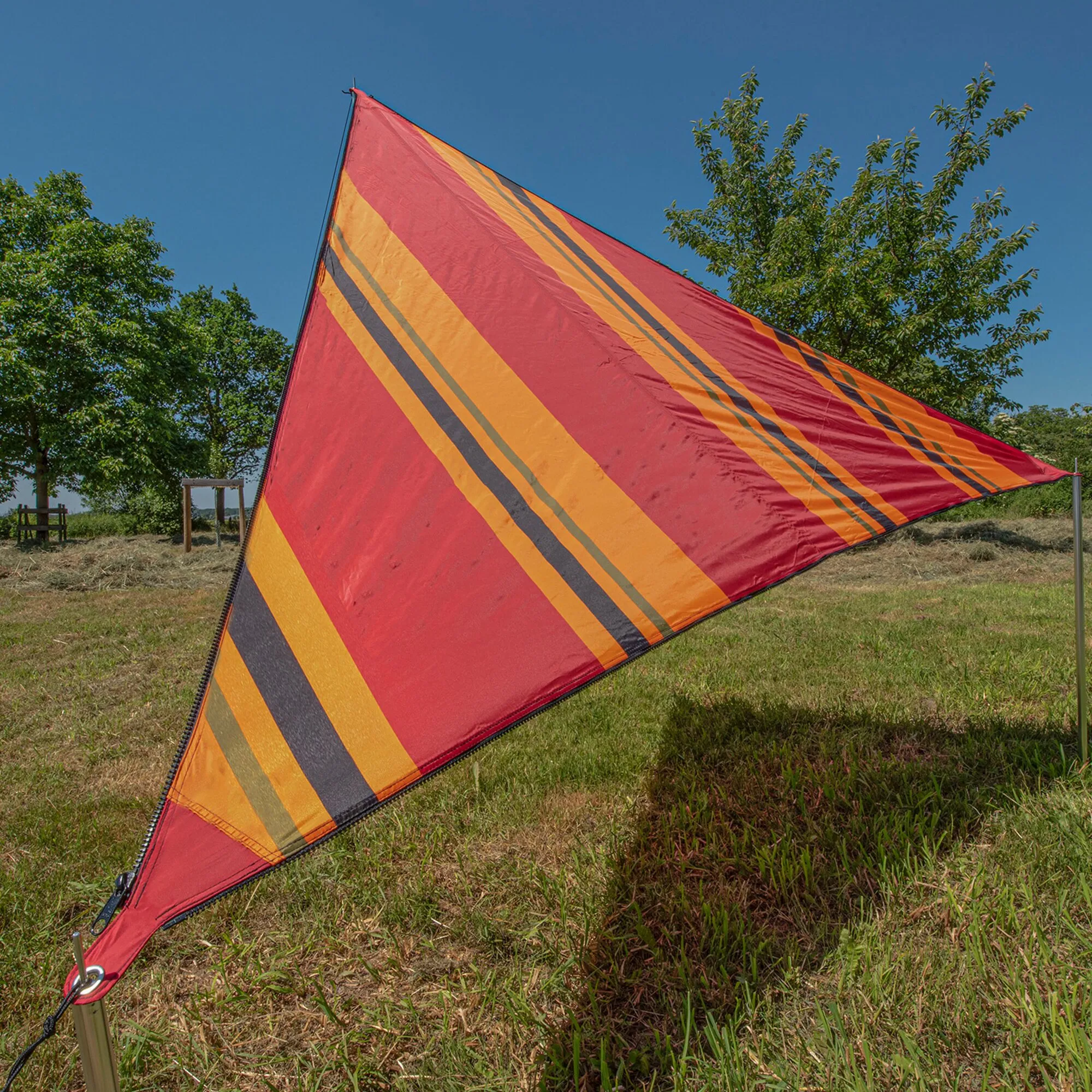 Rotes dreieckiges Sonnensegel Zip Canvas Oriental mit orangefarbenen und dunkelgrauen Streifen, auf einer Wiese gespannt