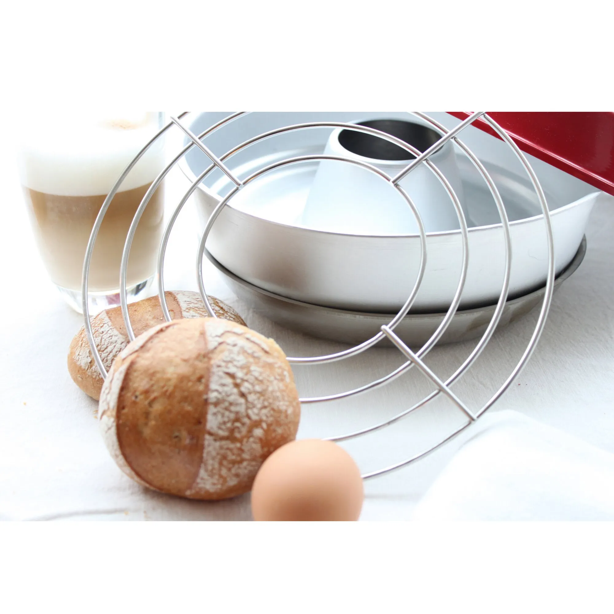 Rundes silberfarbenes Aufbackgitter aus Metall mit 22,5 cm Durchmesser vor Backblech, Brot, Brötchen und Ei