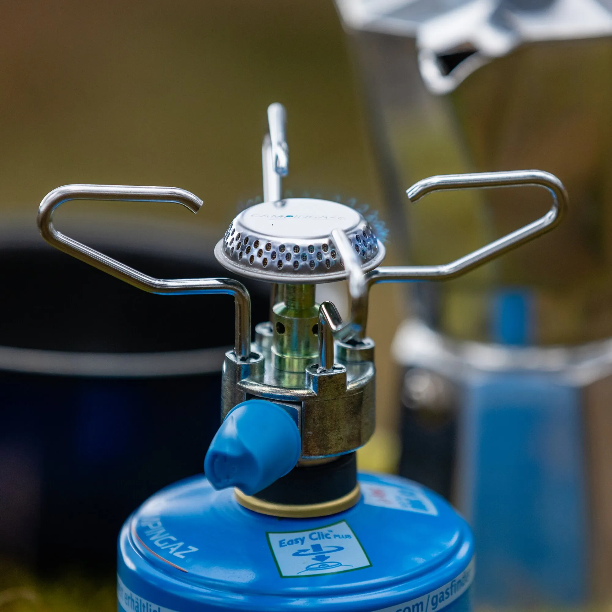 Detailaufnahme des silbernen Gaskochers Bleuet® Micro Plus mit Topfauflage und blauem Gasbehälter im Hintergrund