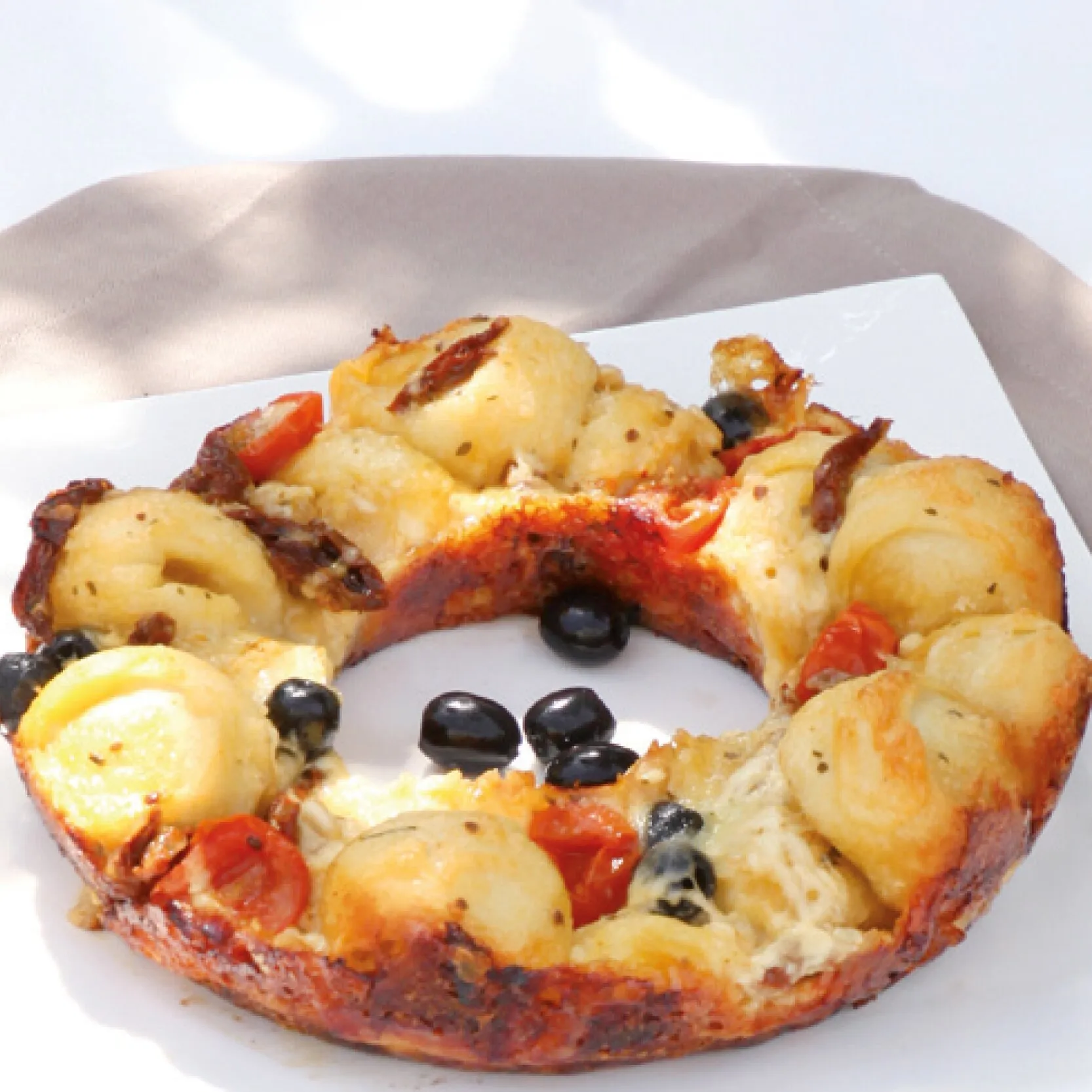 Goldbraun gebackener herzhafter Ringkuchen mit Oliven, Tomaten und getrockneten Tomaten auf weißem Teller aus dem Omnia-Kochbuch