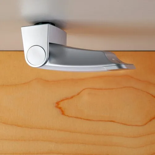 Silberne Combi Spot- und Leselampe Ambience in seitlicher Ansicht, an einer hellen Wand über einer Holzfläche montiert