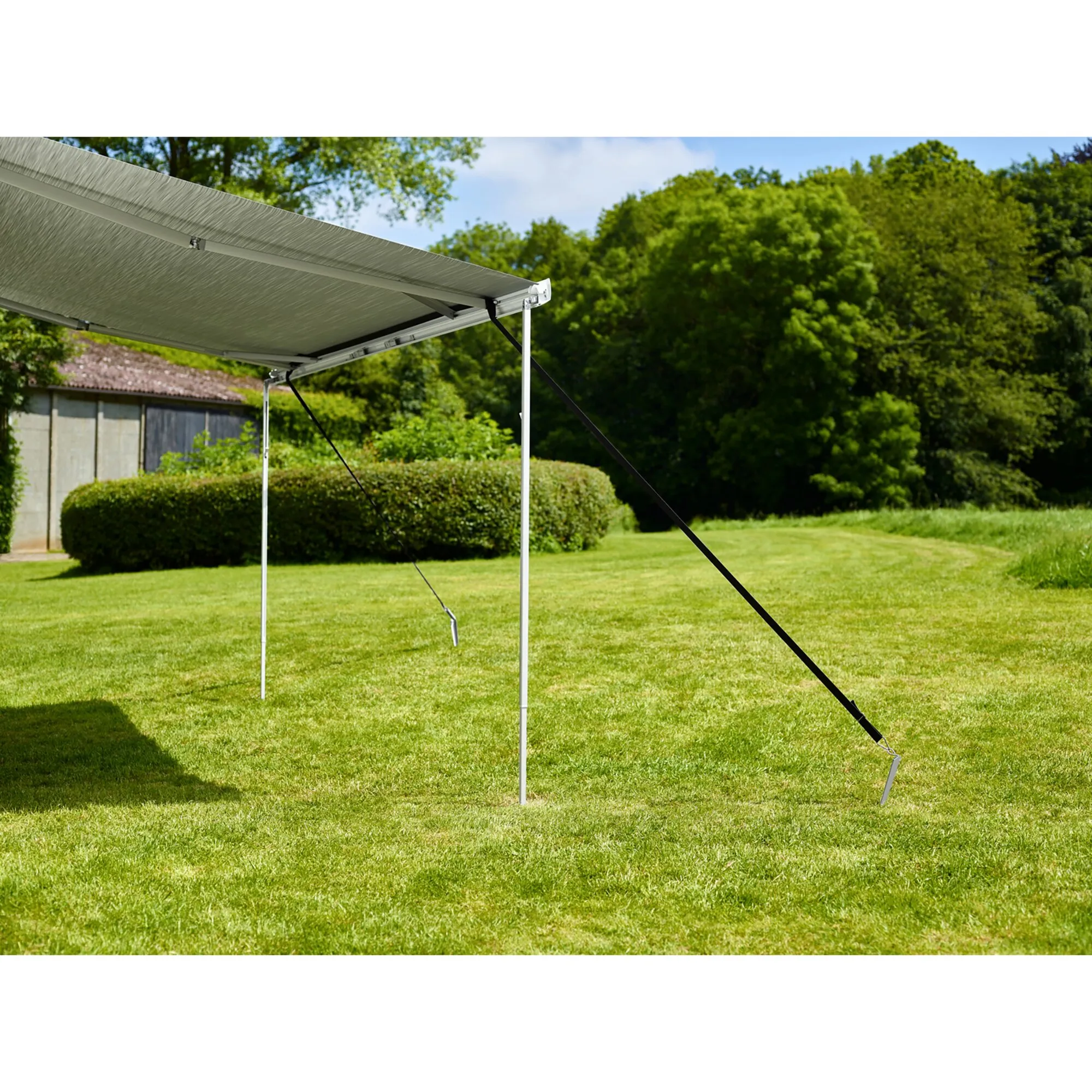 Thule Hold Down Kit mit schwarzen Abspannbändern sichert eine ausgefahrene graue Markise auf einer Rasenfläche mittels Heringen