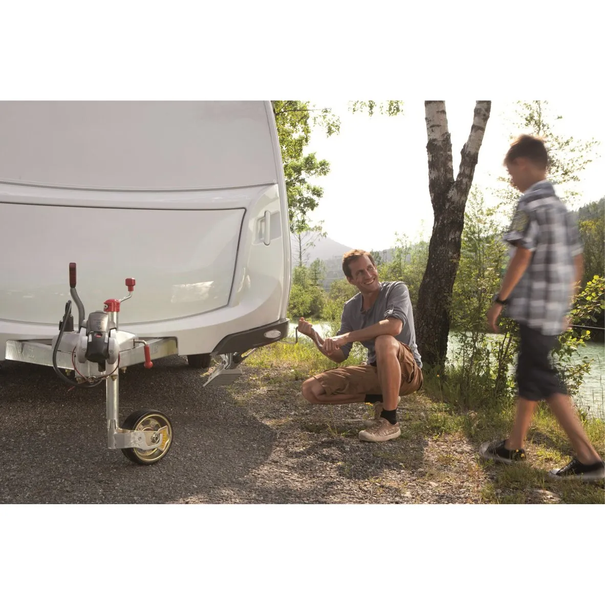 Wohnwagen am See, während ein Mann kniend eine vordere Steckstütze 1250 L mit der Kurbel ausrichtet