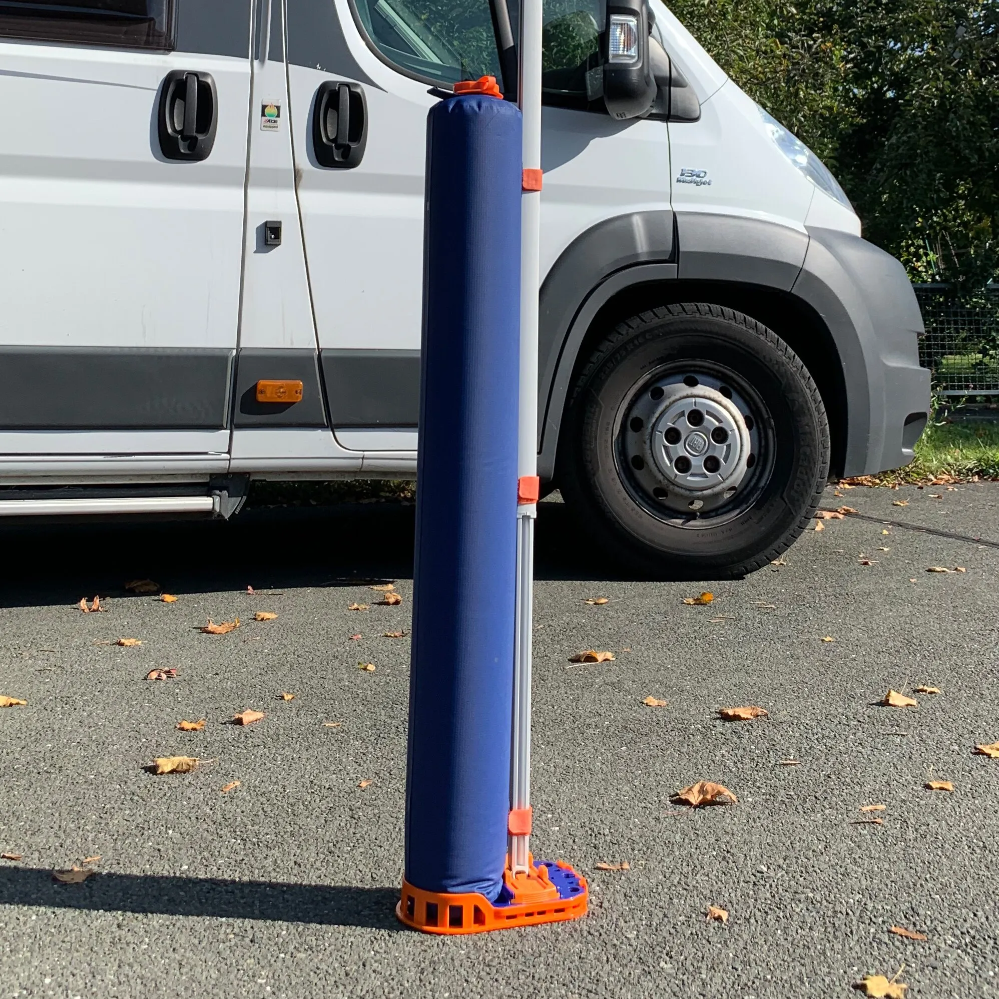Blauer Markisenadapter PP Fix&Go Tube mit orangefarbenen Halterungen neben einem weißen Campervan auf Asphalt