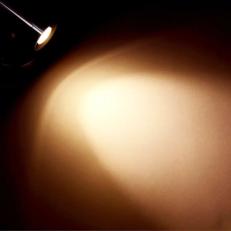 Miniaufbau-Spot LED1x1S22SD mit schwarzem Gehäuse, der einen warmweißen Lichtkegel auf eine Wand projiziert
