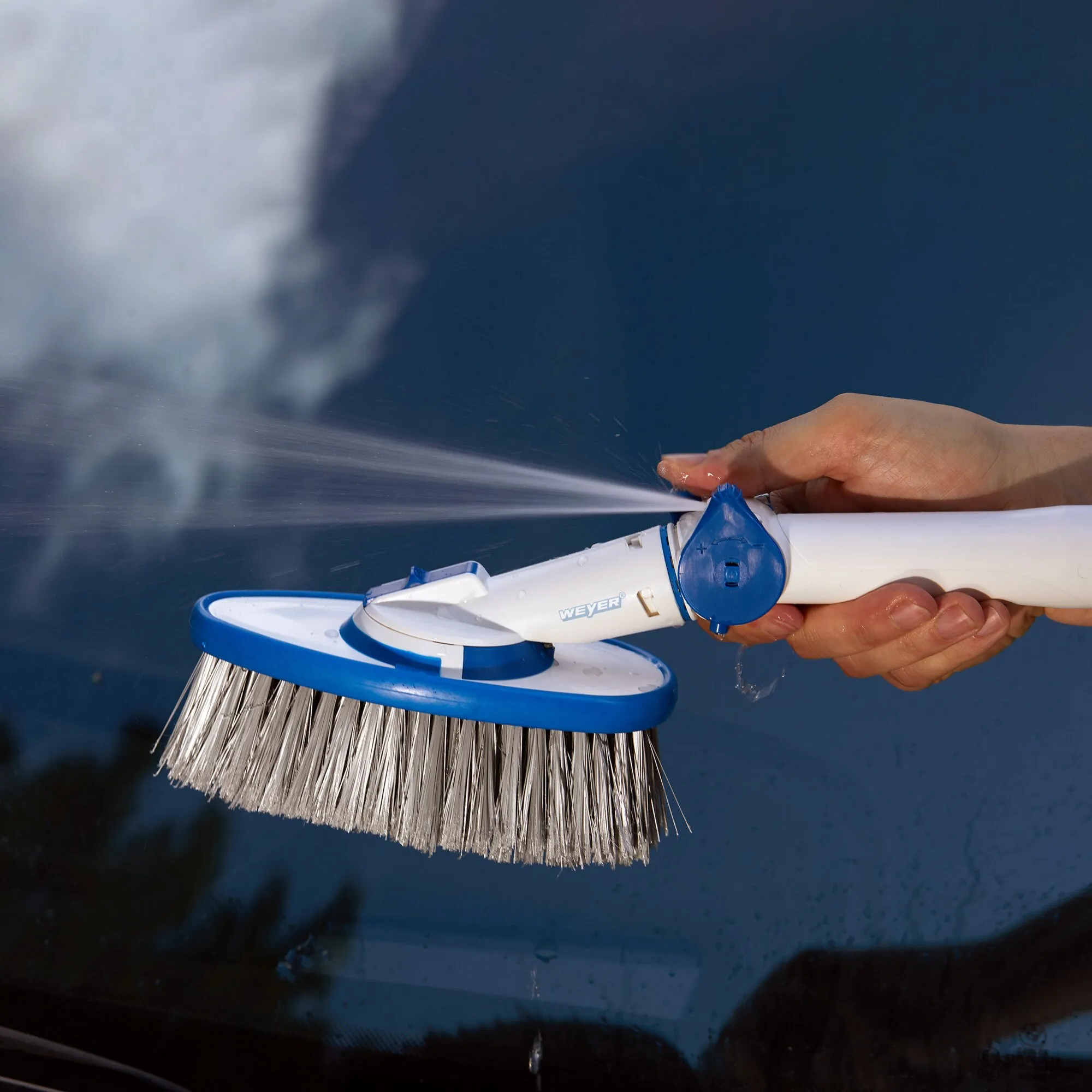 Weiße ovale Waschbürste mit blauem drehbarem Bürstenkopf wird von einer Hand unter fließendem Wasser abgespült