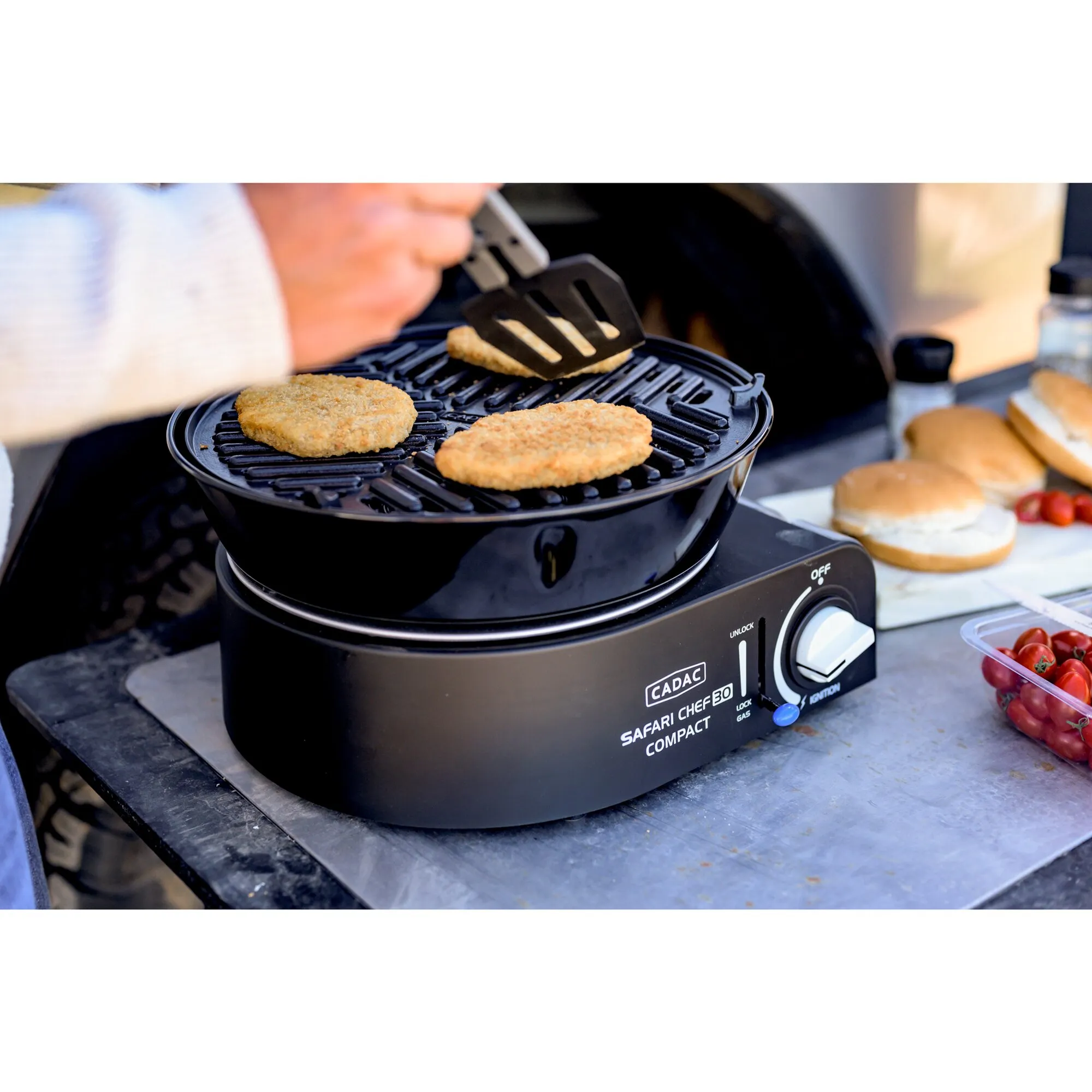 Schwarzer CADAC Safari Chef 30 Compact Gasgrill mit drei Burgerpatties auf dem Rost, während eines mit einem Pfannenwender gewendet wird