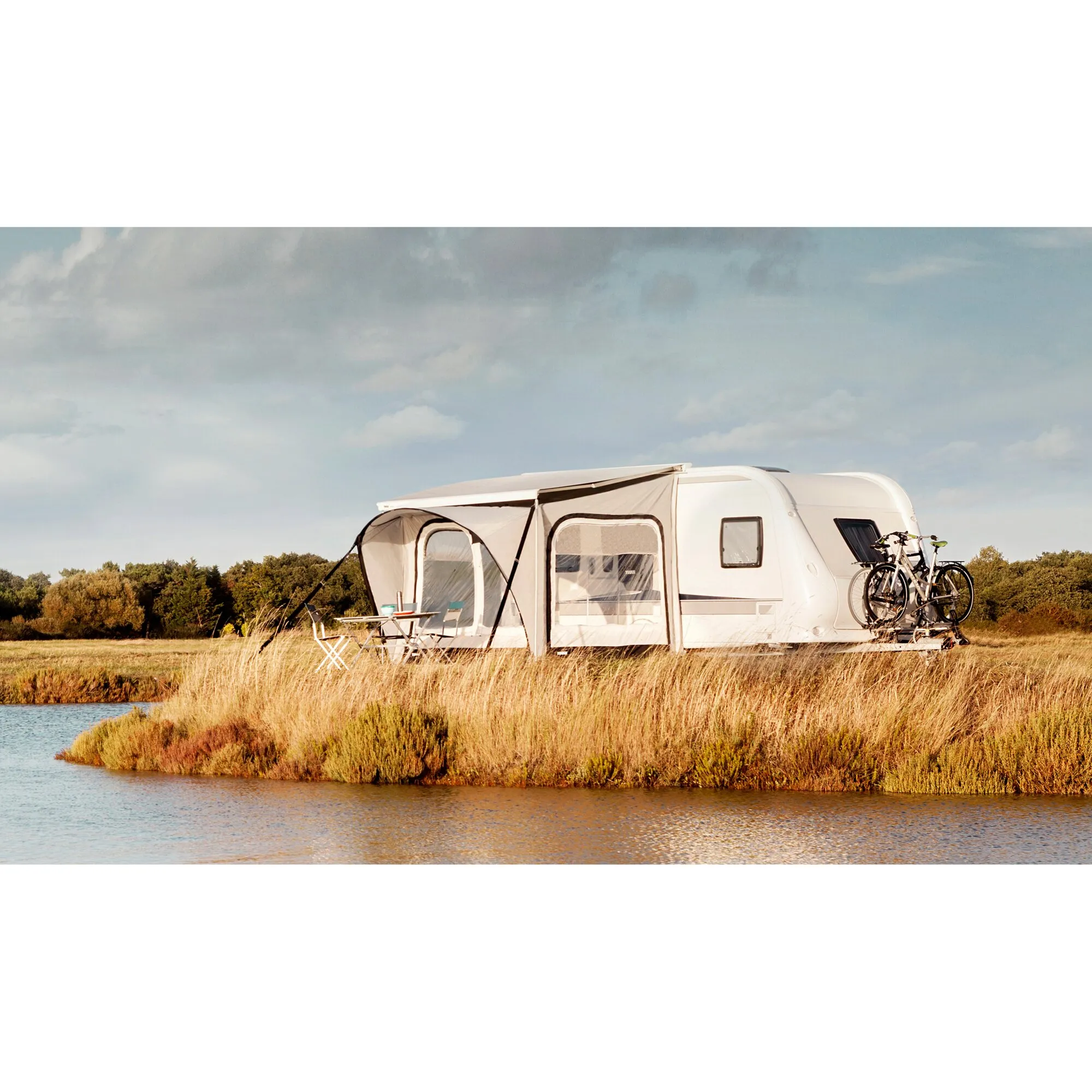 Thule QuickFit Markisenzelt 3,1 x 2,25 m, Höhe M, an weißem Wohnwagen am Wasser mit Tisch, Stühlen und Fahrrädern
