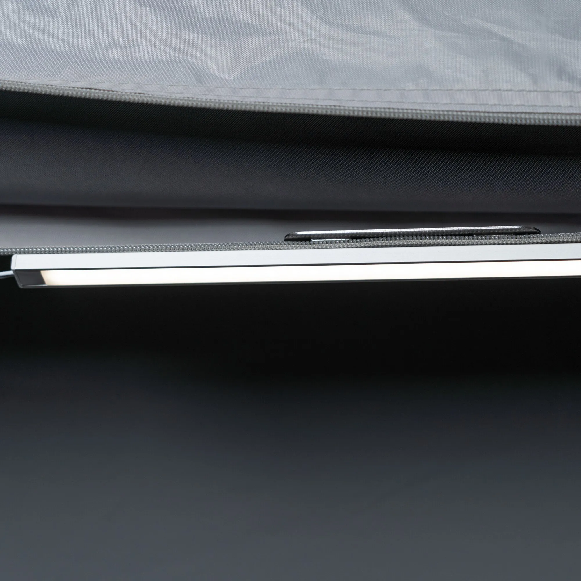 Nahaufnahme einer eingeschalteten LED-Lichtleiste mit schwarzem Gehäuse unter der Stoffkante eines Vorzelts