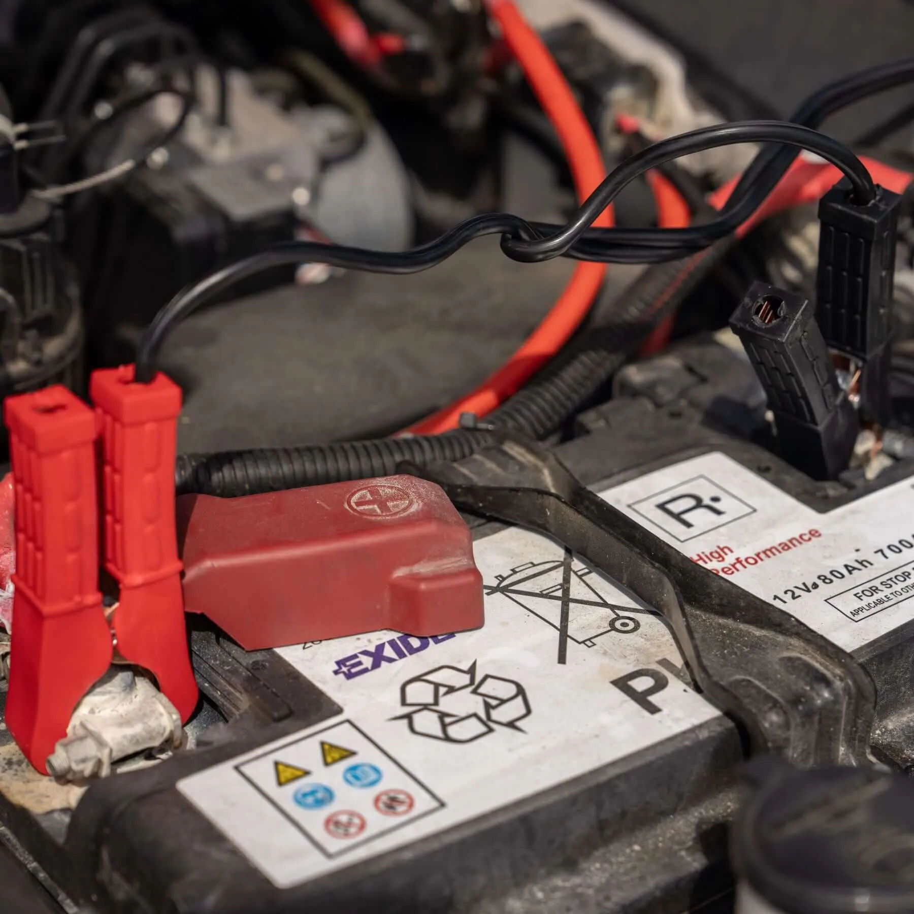 Nahaufnahme einer Kompressor-Box mit schwarzen Kabeln und roten Anschlüssen an einer Autobatterie im Motorraum