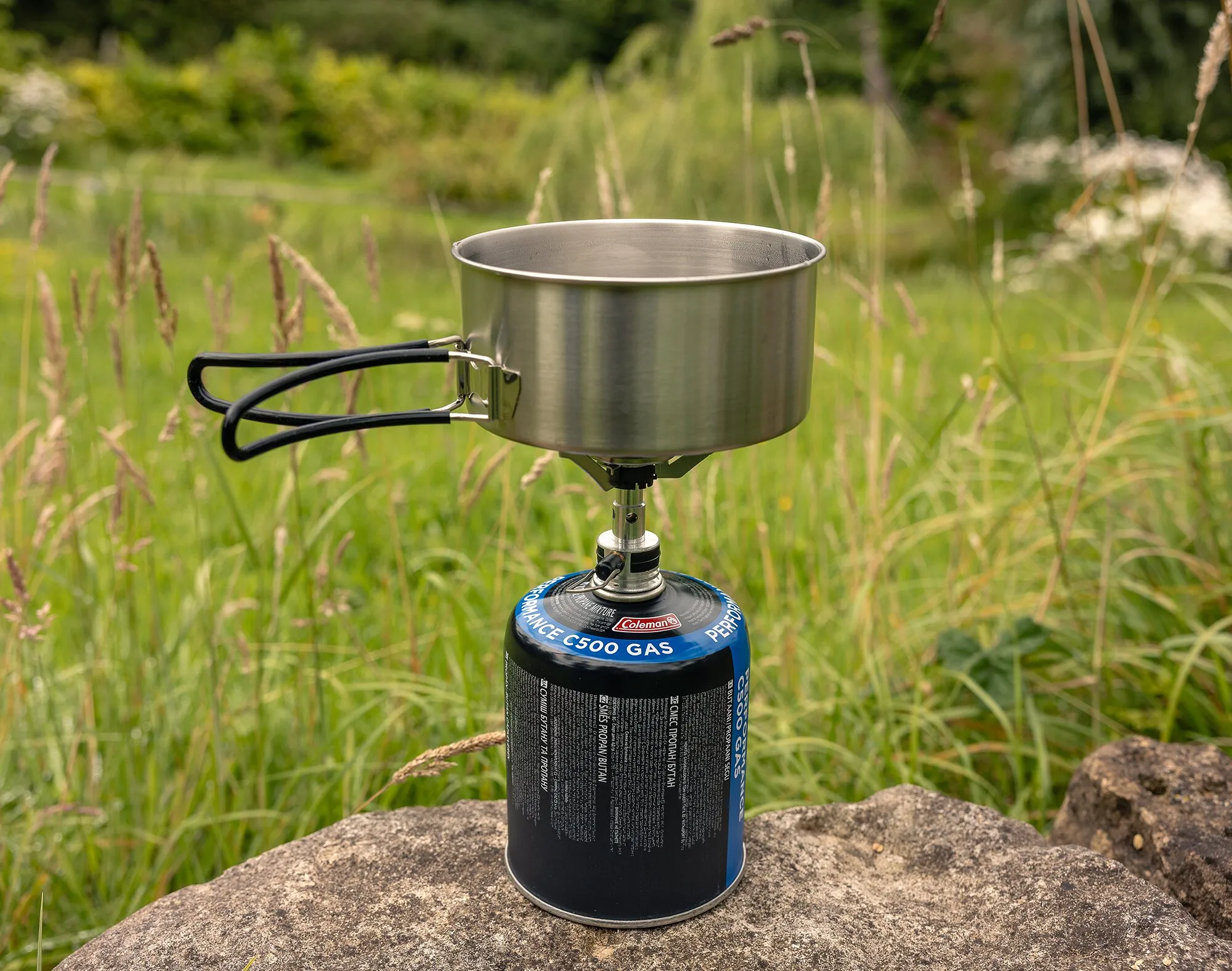 Edelstahltopf mit schwarzen Klappgriffen auf einem Gaskocher im Trekking-Kochgeschirrset, im Freien auf einem Felsen grasXitsonga