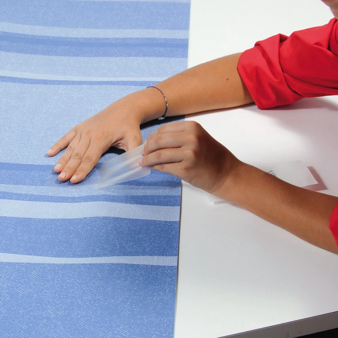 Anwendung des Kits Repair Plus: Eine transparente Folie wird auf eine Hand auf einer blauen Unterlage aufgebracht