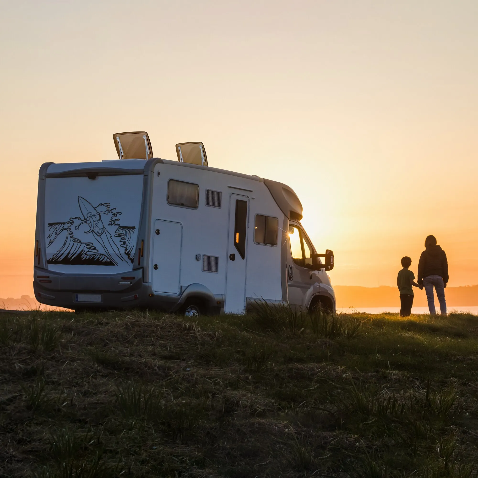 Wohnmobil mit zwei geöffneten roofSTAR-4-Dachhauben mit Zwangsbelüftung bei Sonnenuntergang, daneben stehen zwei Personen