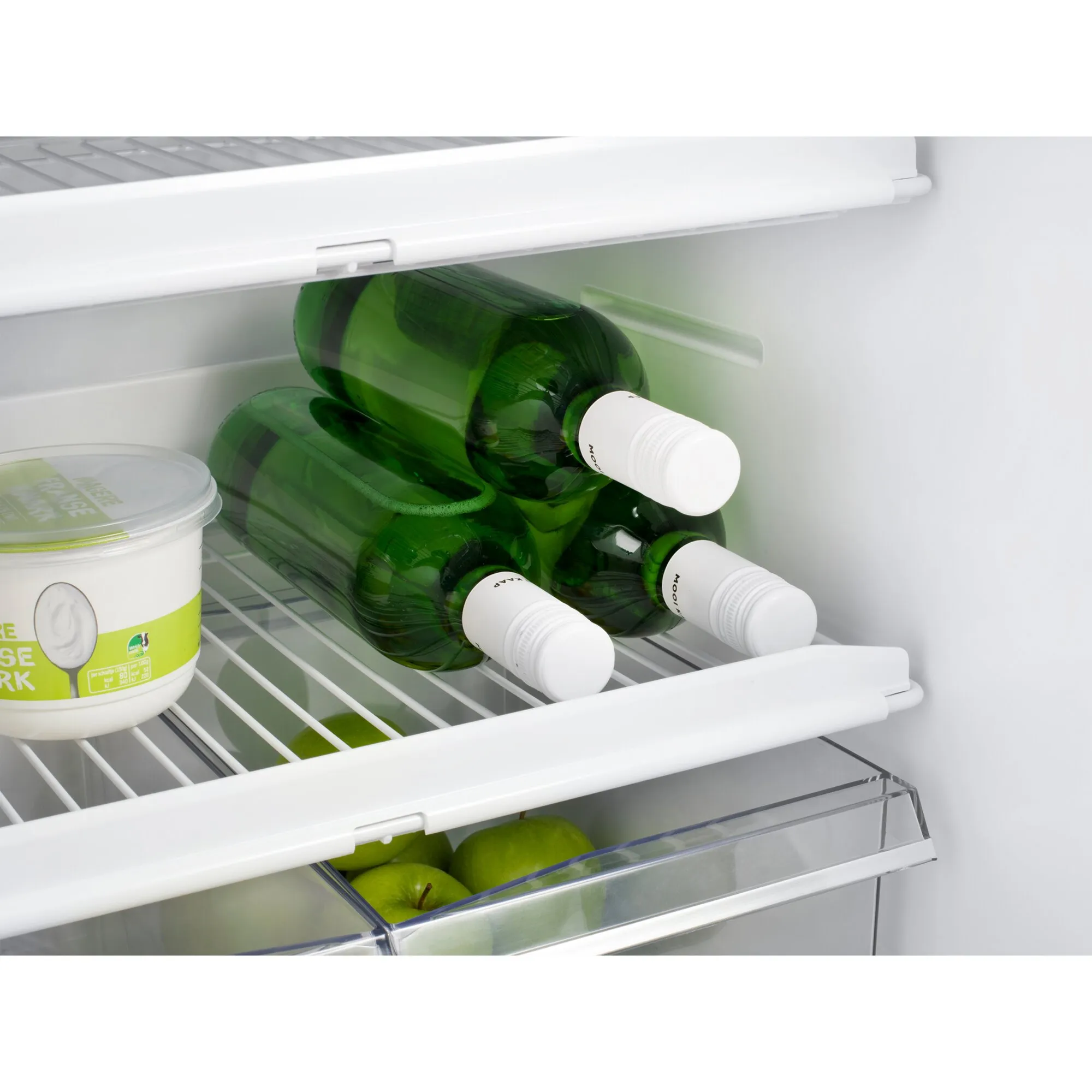Innenansicht des Kühlschranks T2175 mit drei grünen Flaschen, Joghurtbecher, Gitterablagen und Obstfach mit Äpfeln