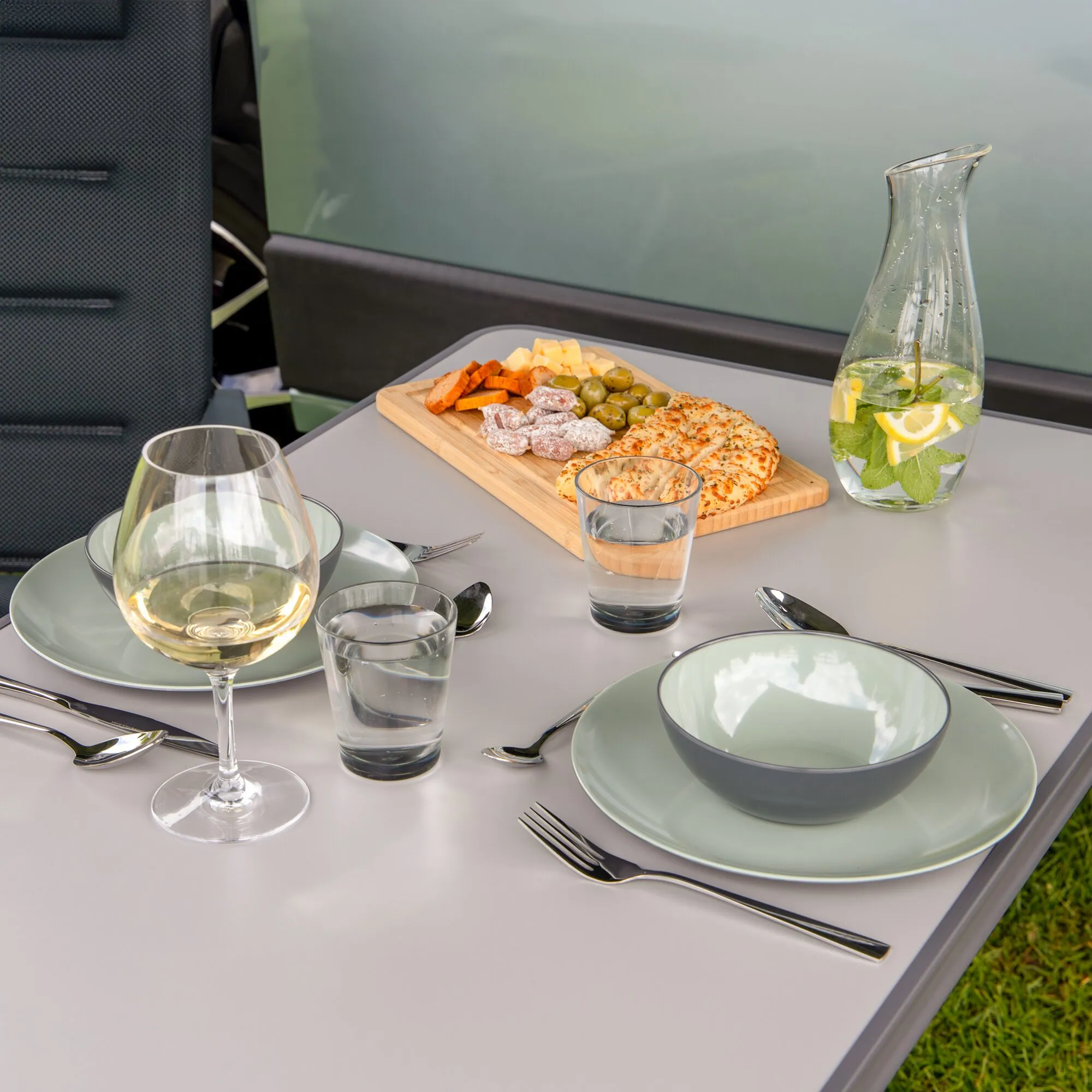 Hellgrünes Geschirrset Vivid Line mit Tellern und Schalen auf einem gedeckten Tisch im Fahrzeug, dazu Gläser, Besteck und Snacks
