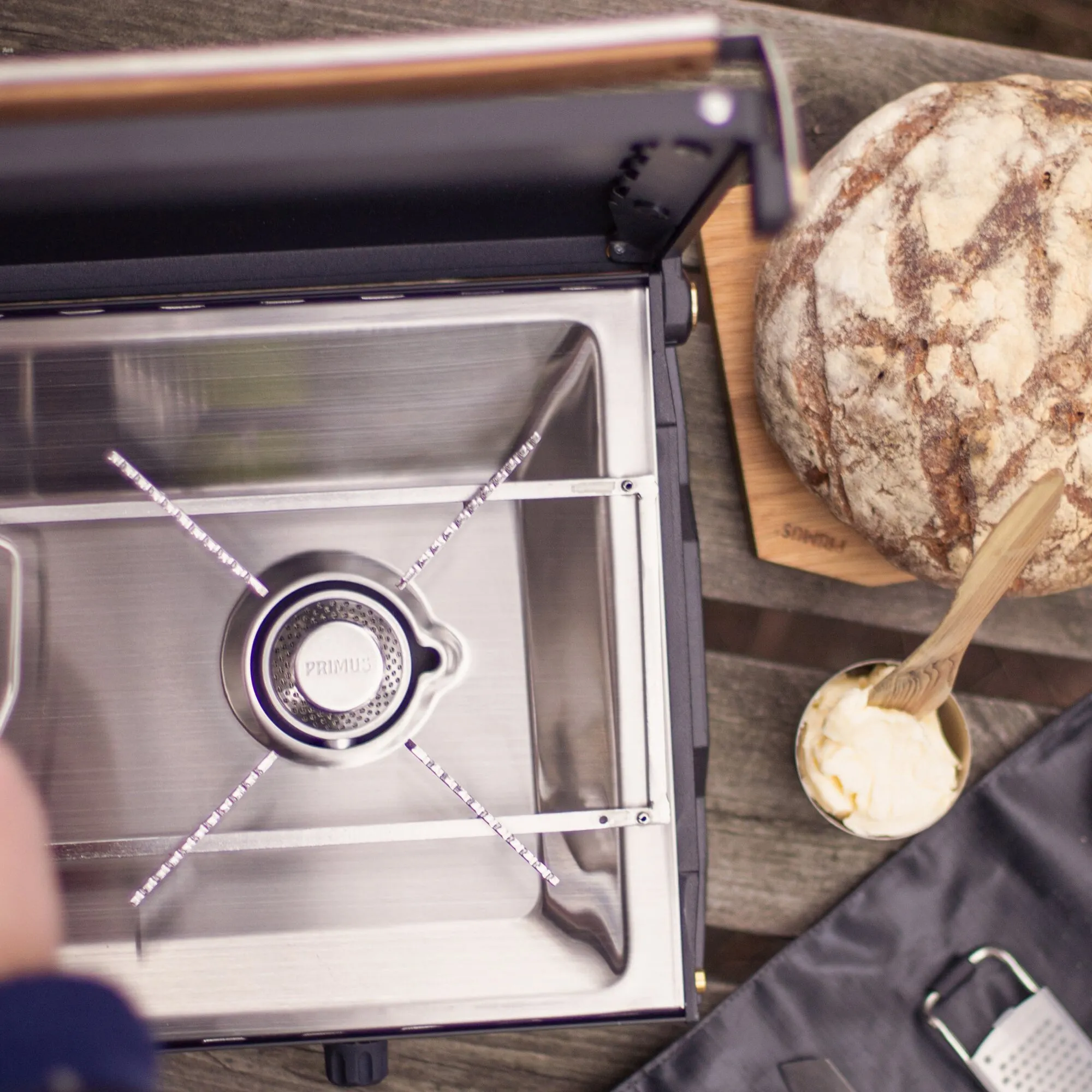 Geöffneter Primus Kinjia Gaskocher aus Edelstahl mit einem sichtbaren Brenner neben Brot und Schüssel mit Teig