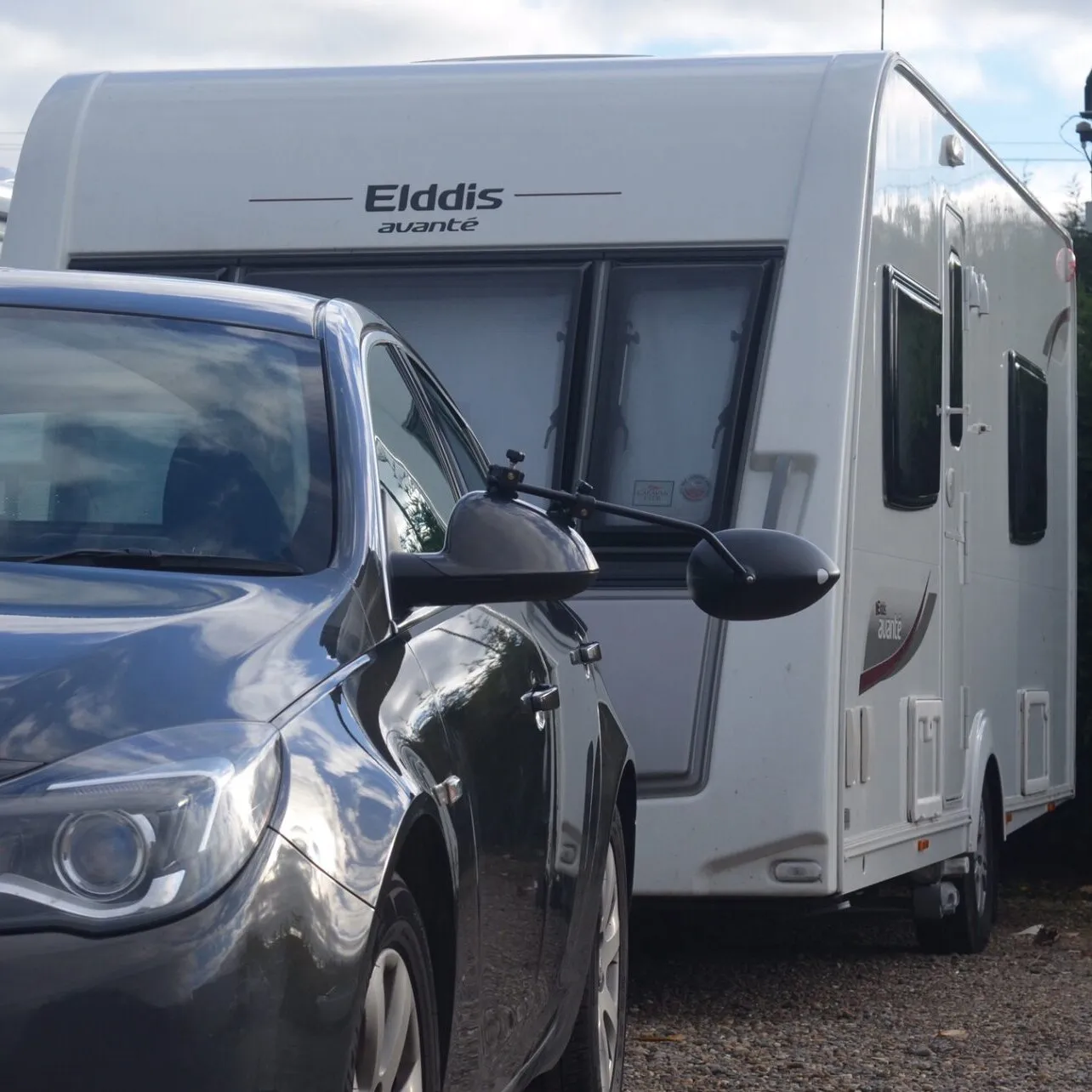 Schwarzer Caravanspiegel Aero 4 Mirror Convex XL am Außenspiegel eines Autos vor einem weißen Elddis-Wohnwagen montiert