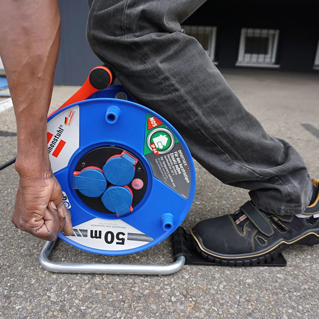 Person tritt auf den Metallbügel einer blauen Kabeltrommel, um sie mit dem Trommeltritt standfest zu fixieren