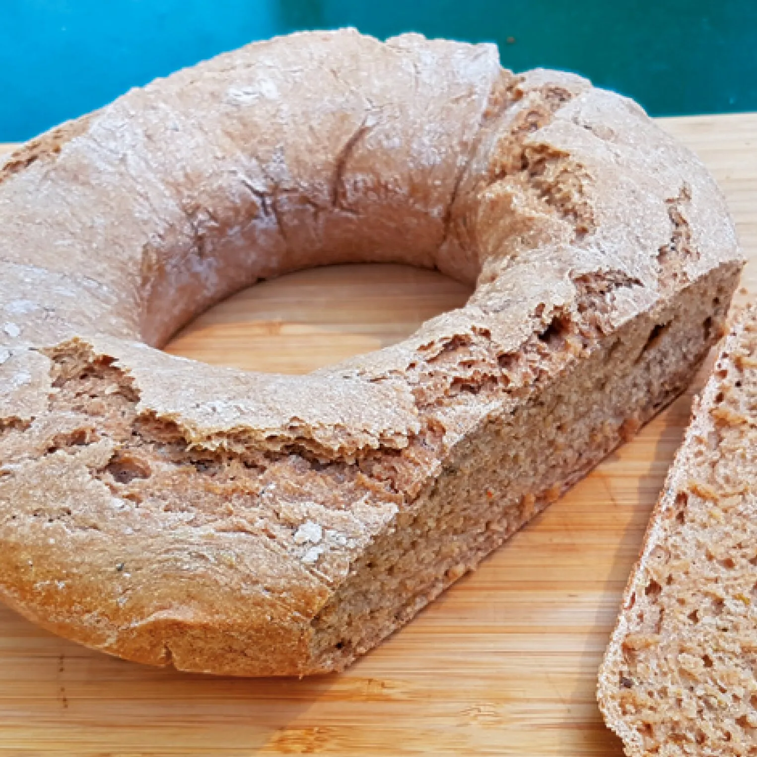 Rustikales, ringförmiges Vollkornbrot mit aufgeschnittener Scheibe auf einem Bambusbrett – Rezeptmotiv für das Omnia-Backbuch