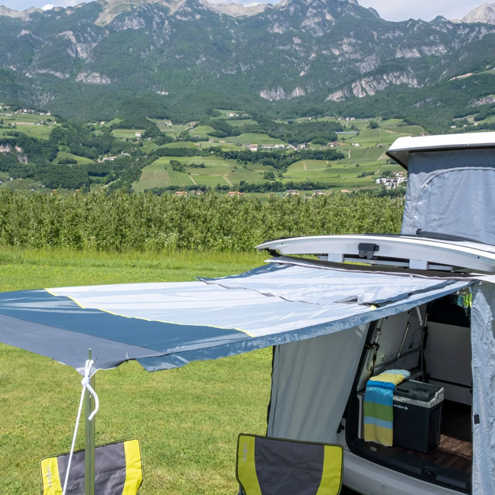 Geöffnetes blau-graues Heckzelt Pilote Caddy 4 am Fahrzeug mit Innenraum, Abspannleinen und Berglandschaft im Hintergrund