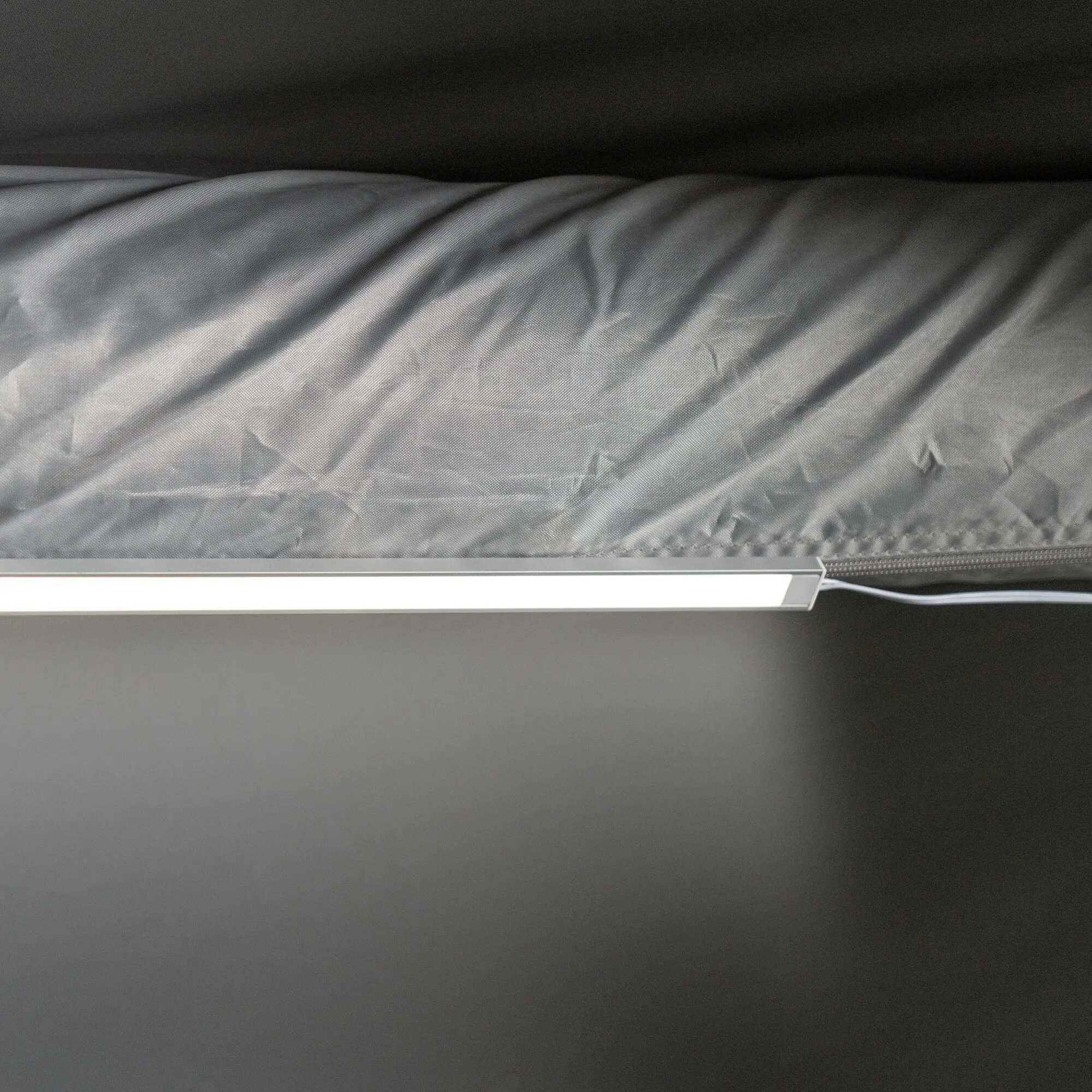 Beleuchtete LED-Lichtleiste in weißem Gehäuse an grauem Vorzeltstoff, mit Anschlusskabel und Reißverschluss im Detail sichtbar