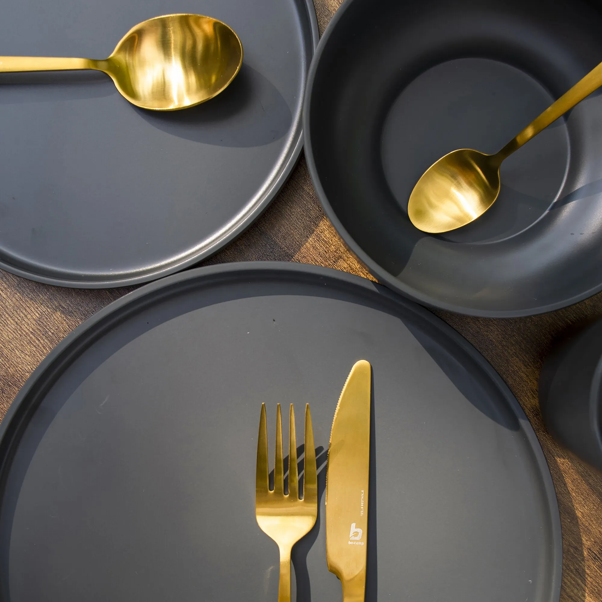 Goldenes Fairbanks Besteck-Set mit Löffeln, Gabel und Messer auf dunkelgrauen Tellern angerichtet