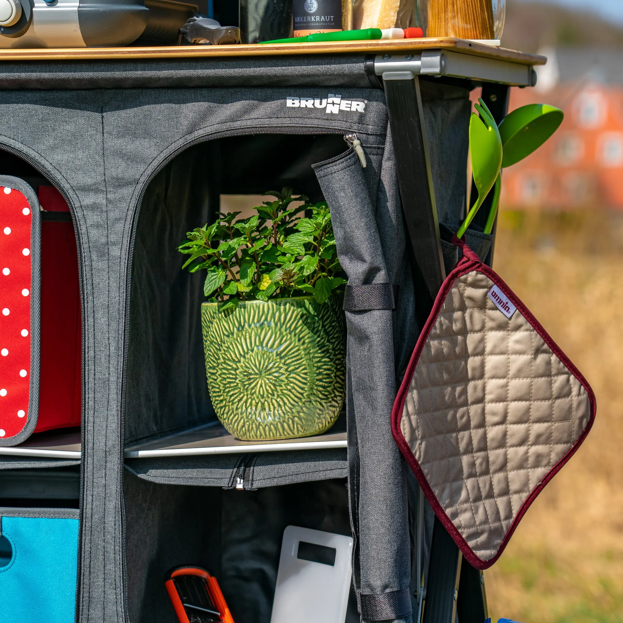 Beiger, rautenförmig gesteppter Topflappen mit dunkelroter Einfassung, an einem Campingküchenwagen hängend