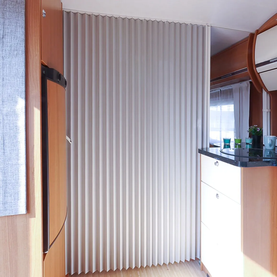 Flexibler Raumteiler REMIform I als hellbeige, vertikal gefaltete Trennwand in einem Wohnmobil-Interieur