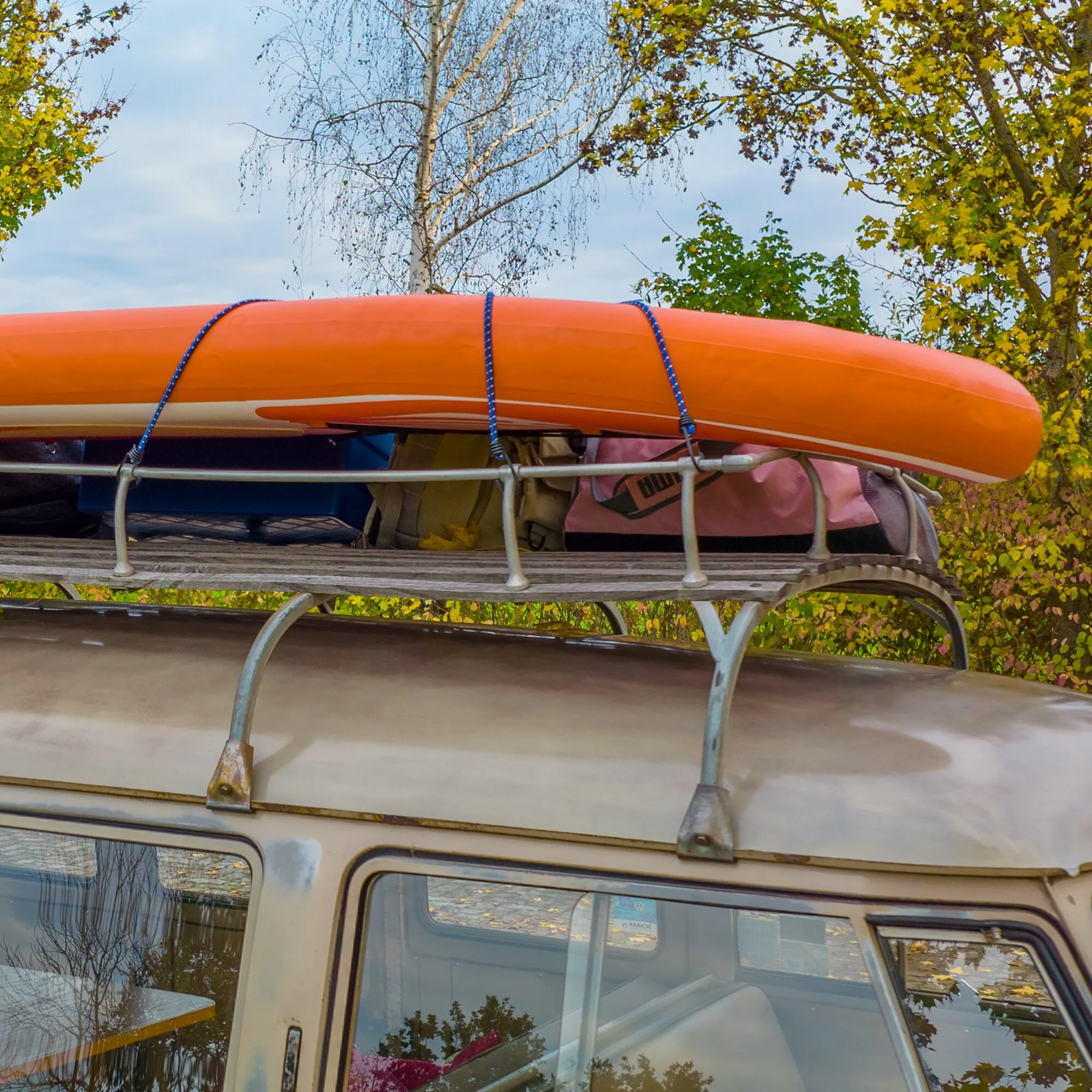Blaue Gepäckspinne sichert ein orangefarbenes Schlauchboot und weiteres Gepäck auf dem Dach eines Fahrzeugs