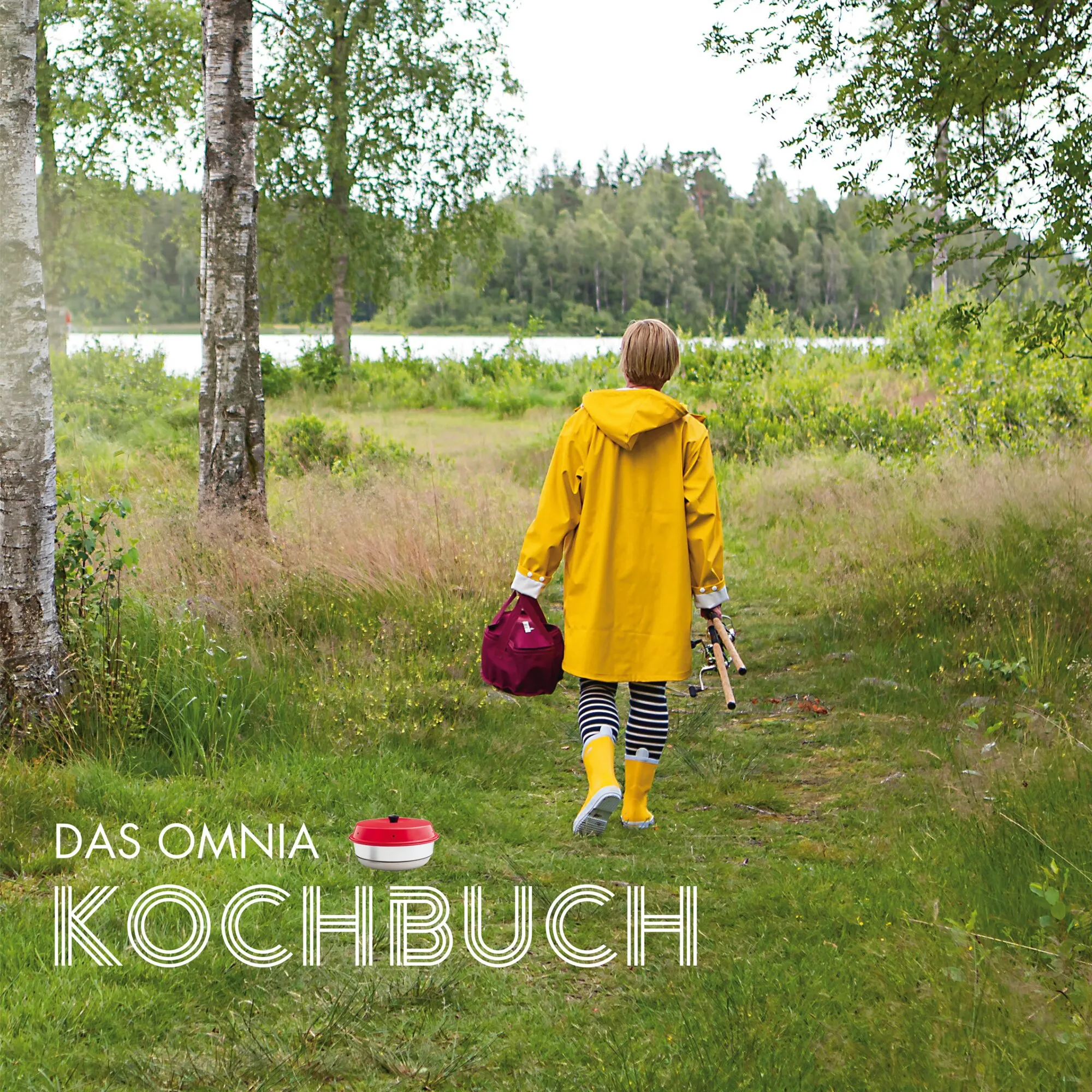 Omnia Kochbuch mit einer Person im gelben Regenmantel am See und sichtbarem roten Omnia-Backofen im Gras