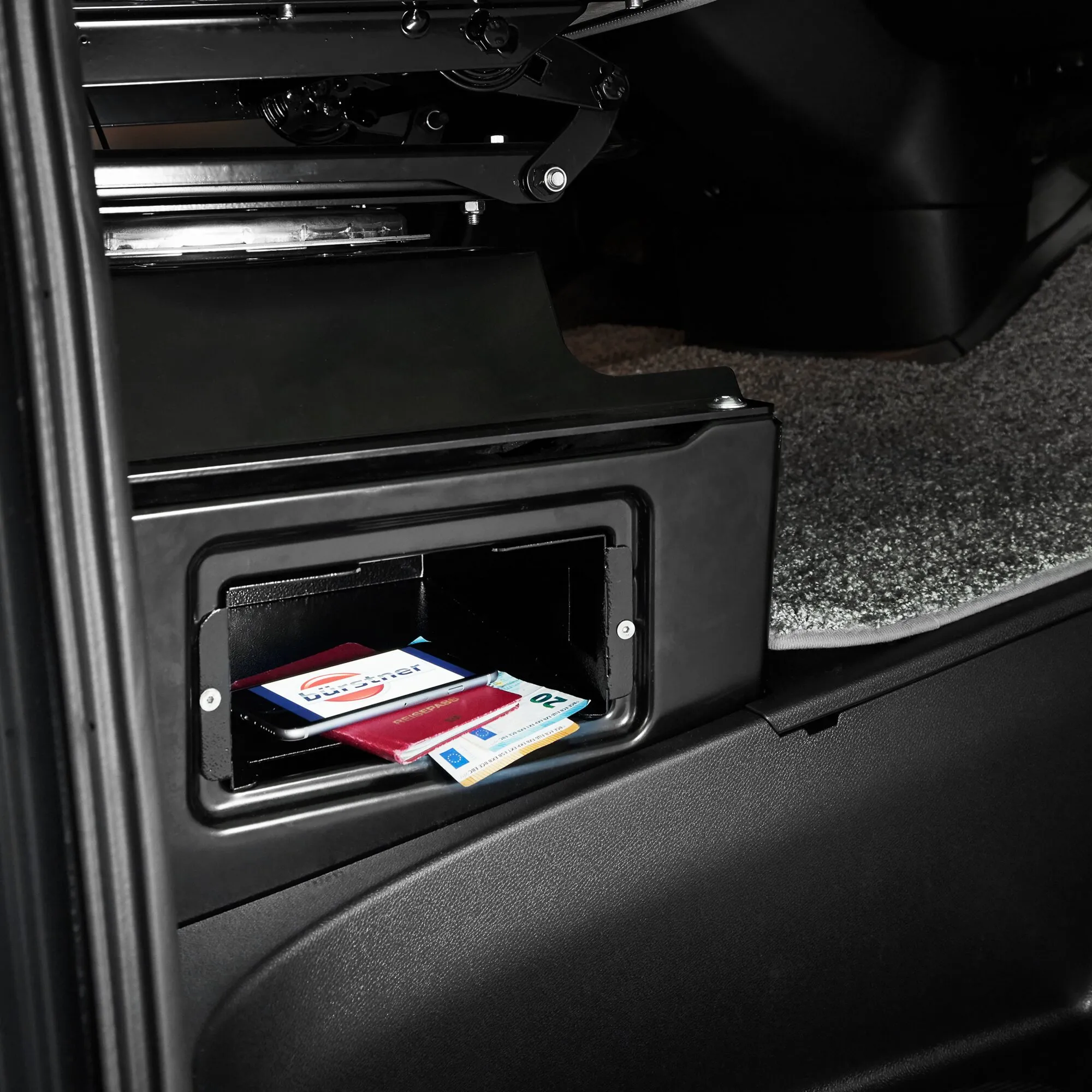 Geöffneter schwarzer Sitzsockelsafe im Mercedes-Benz Sprinter mit ausgeklapptem Sitzgestänge und Fach für Smartphone sowie Dokumente