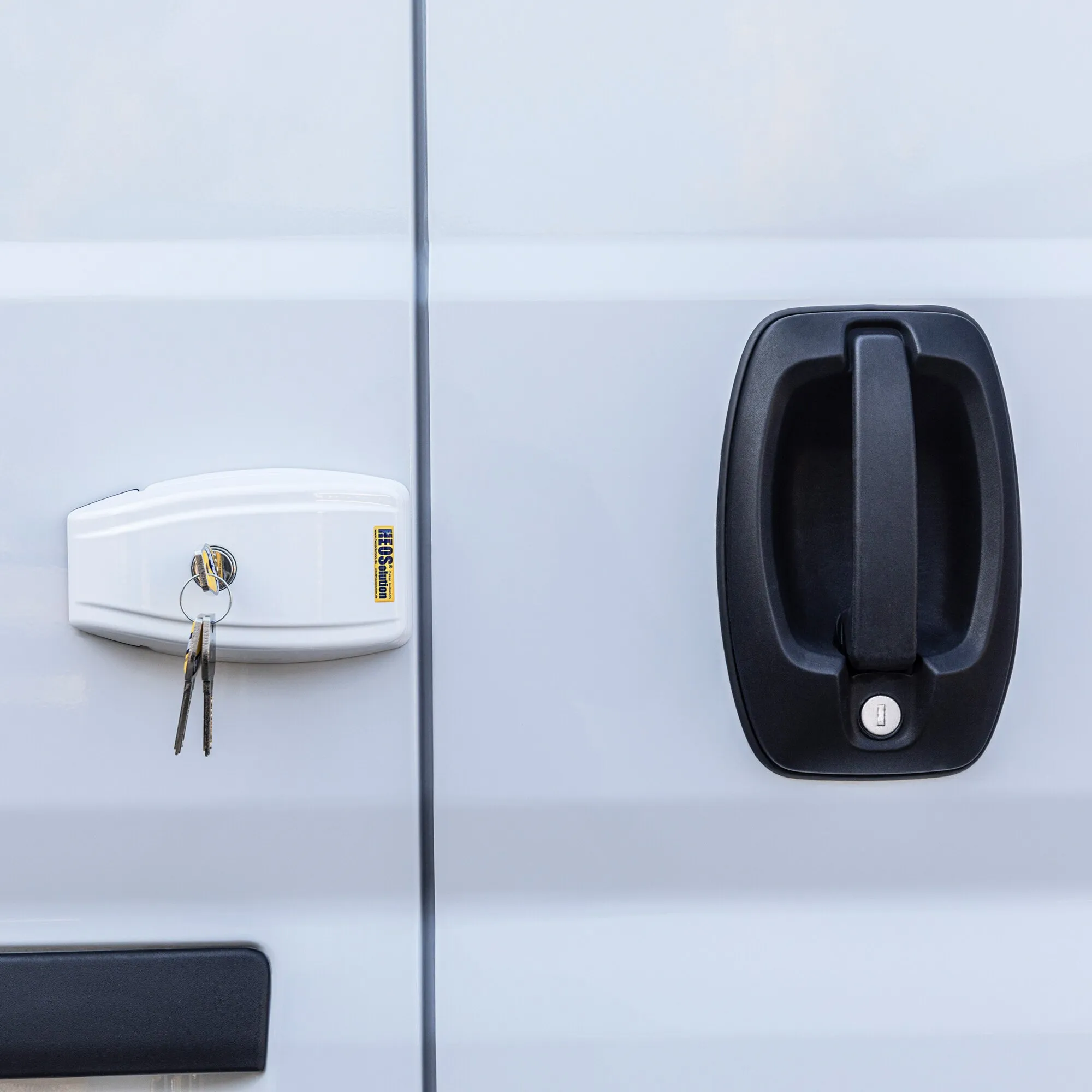 Weiße HEOSafe Van Security Türsicherung an der Hecktür eines Vans mit eingestecktem Schloss und zwei herabhängenden Schlüsseln