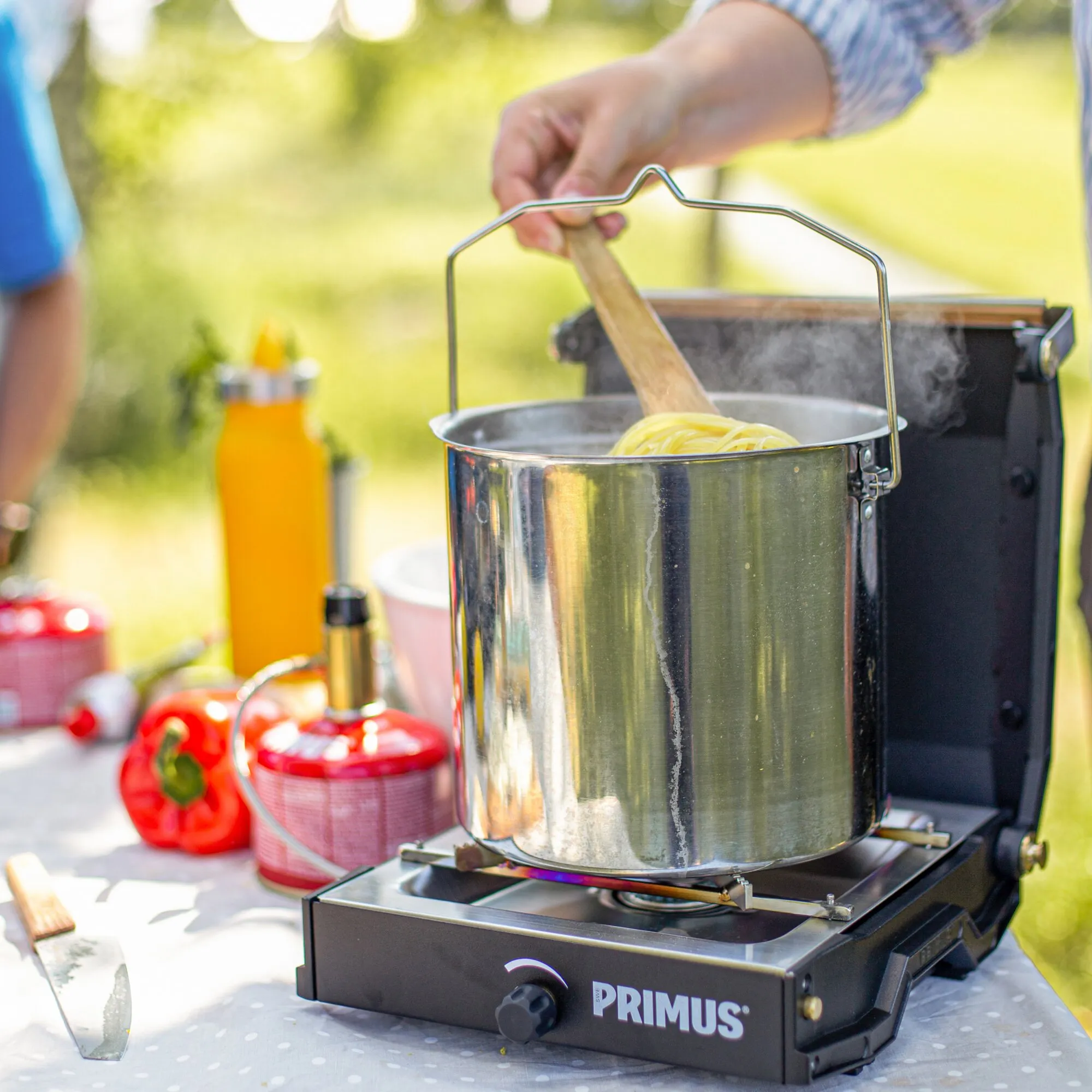 Schwarzer Primus Moja Stove mit großem Edelstahltopf und Pasta, während eine Person beim Kochen im Freien umrührt