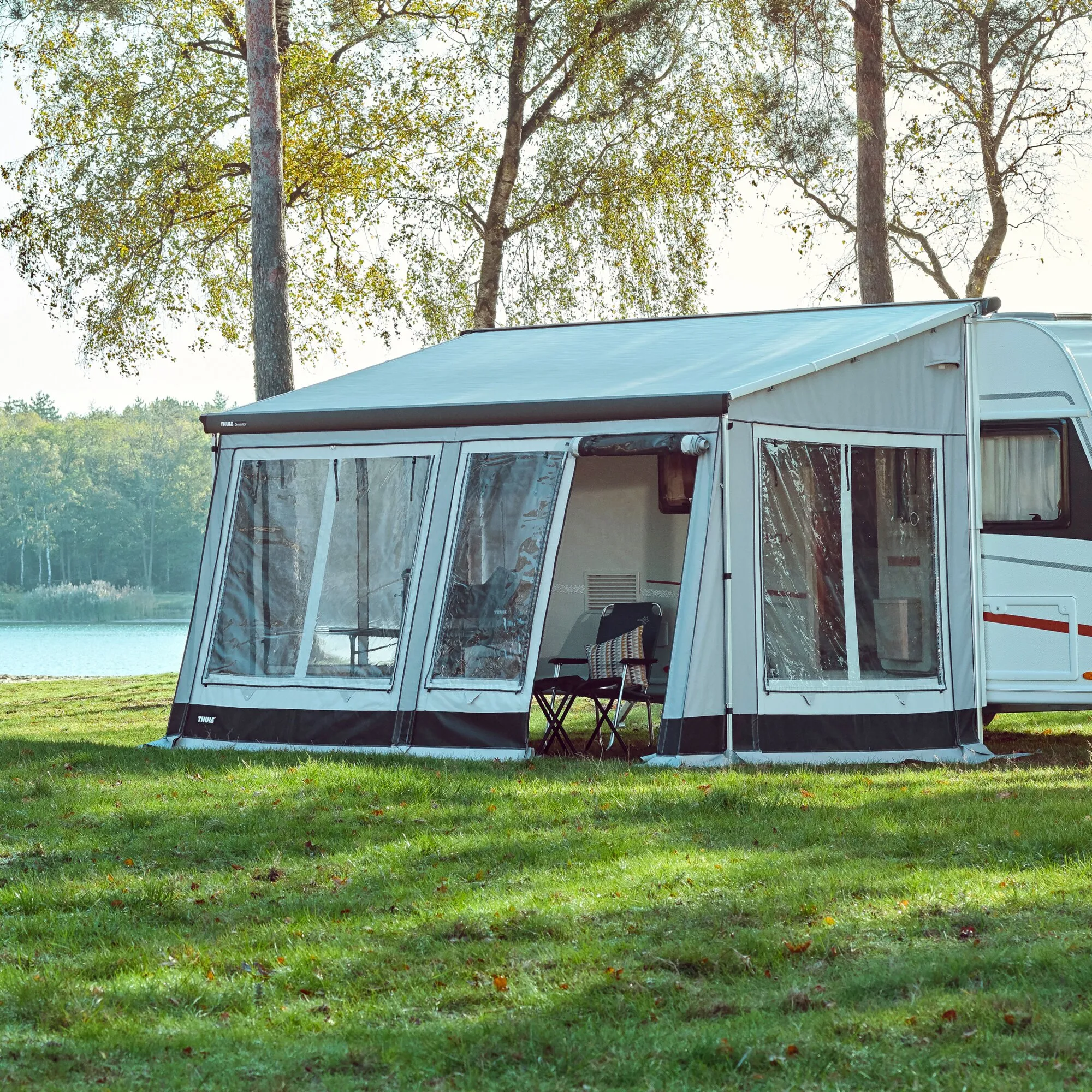 Graues Markisenzelt Thule Veduta mit transparenten Fenstern an einem Wohnwagen auf einer Wiese am See