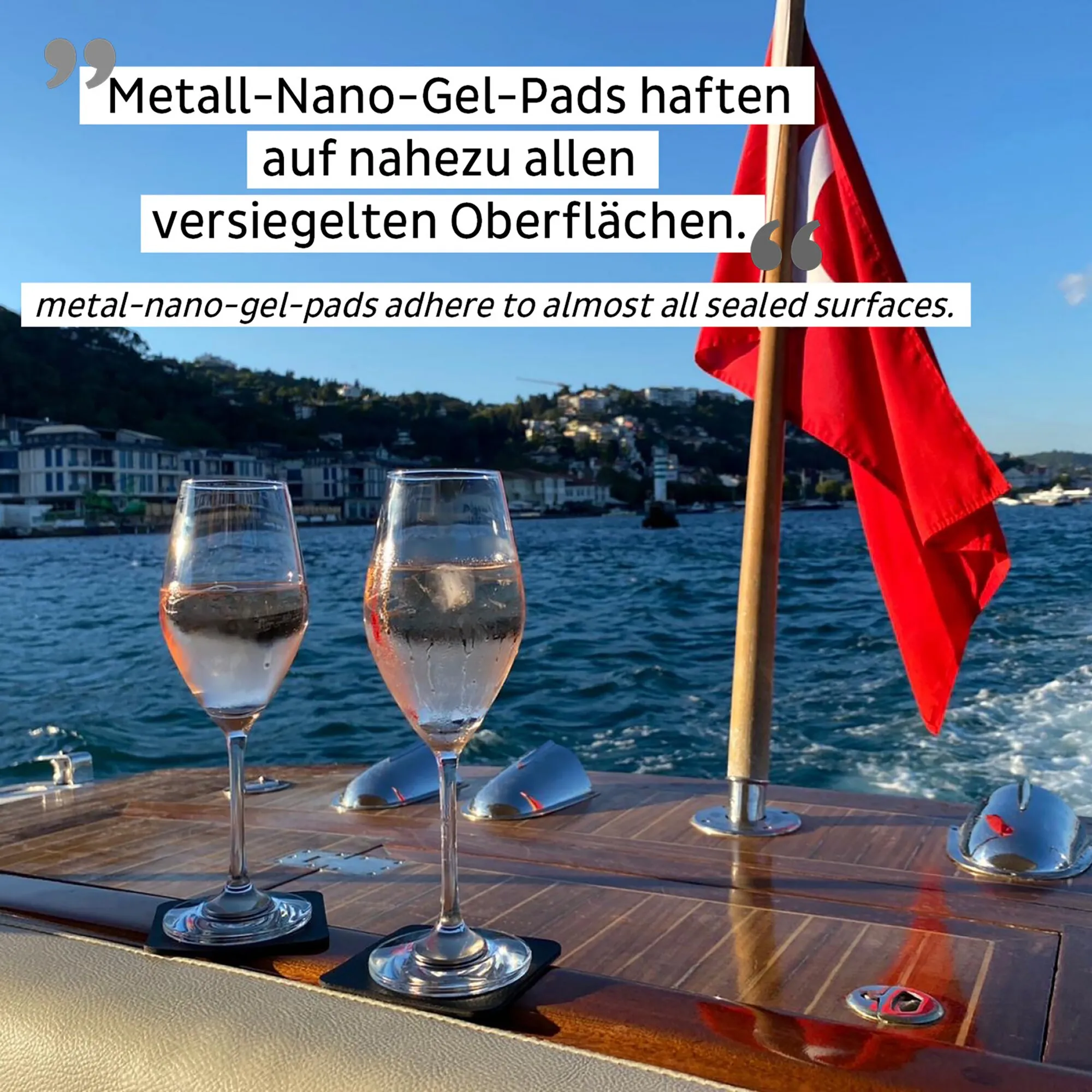 Zwei transparente Magnet-Kristallgläser mit langem Stiel stehen auf schwarzen Pads auf einer Yacht vor Küste und roter Flagge