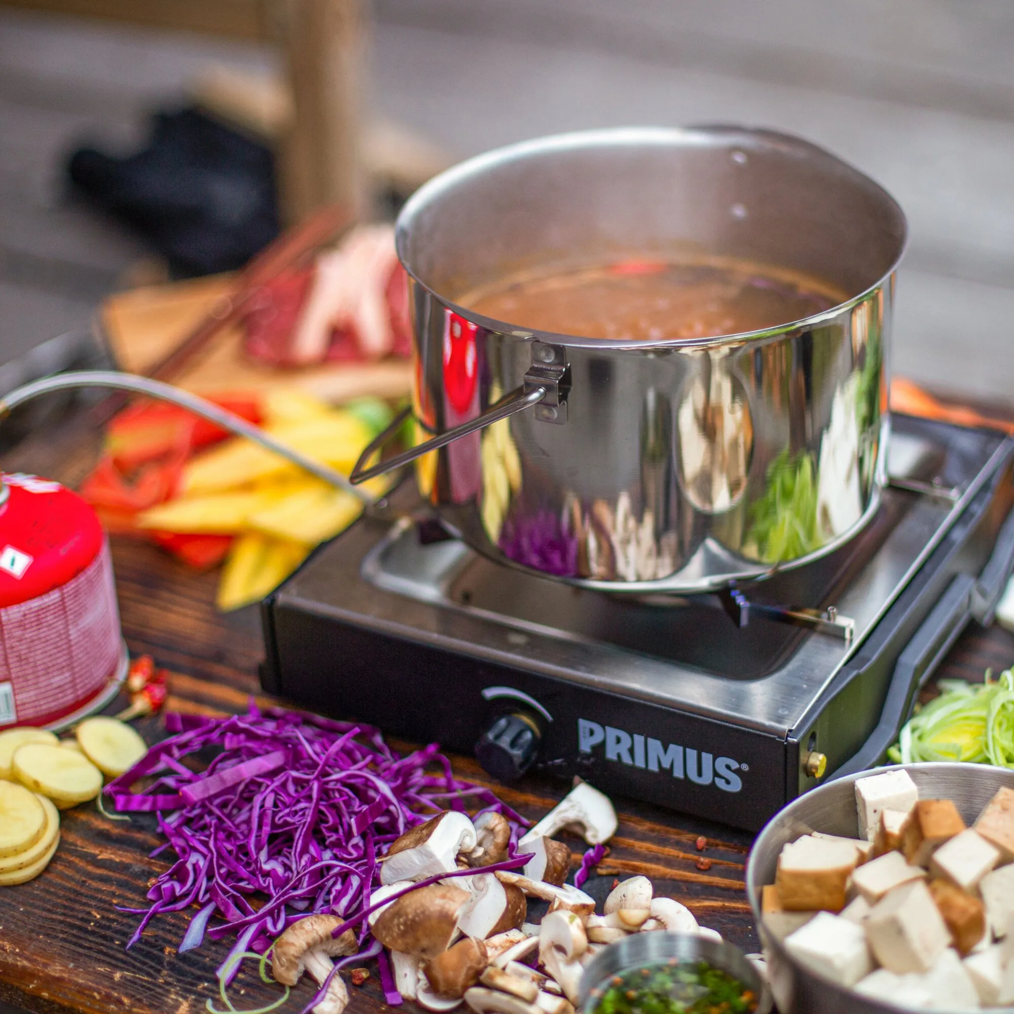 Schwarzer Gaskocher Primus Moja Stove mit Edelstahlkochtopf beim Kochen, umgeben von vorbereitetem Gemüse
