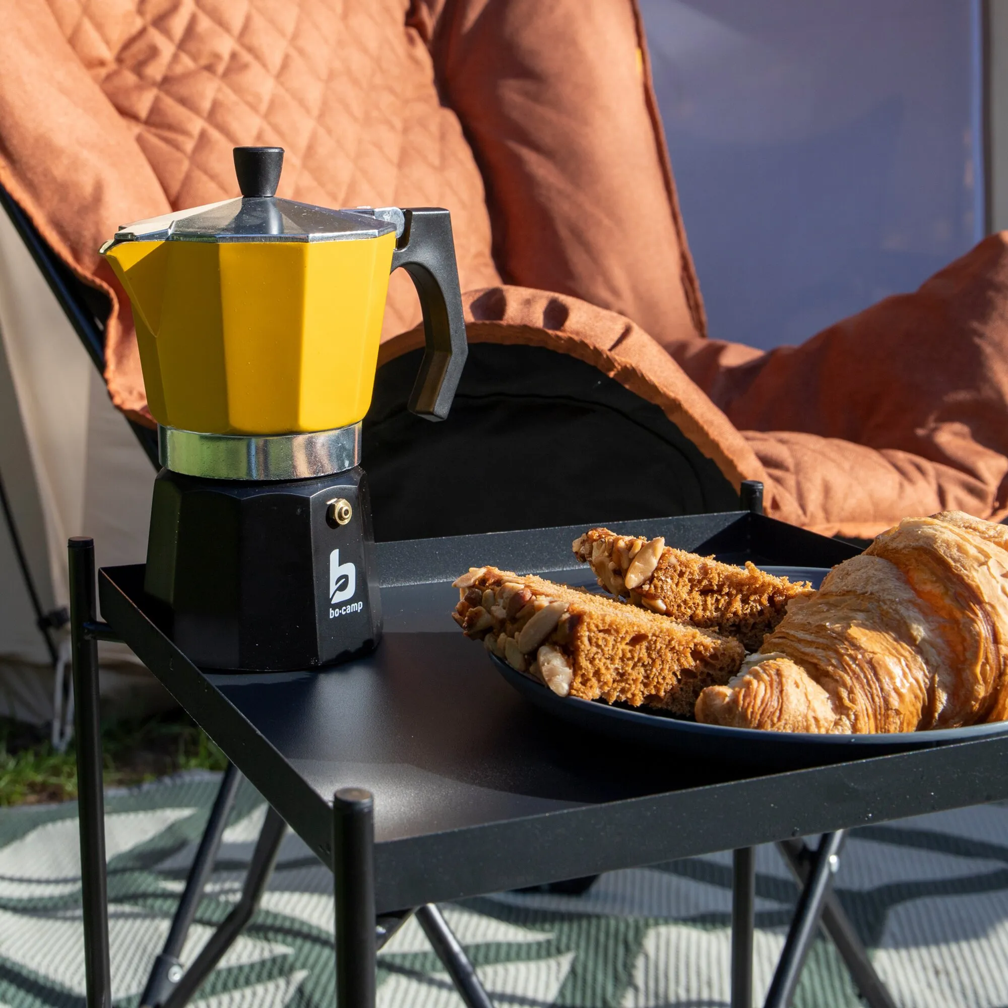 Gelber Kaffeebereiter Hudson mit schwarzem Griff und Metalldeckel auf einem Campingtisch neben Gebäck