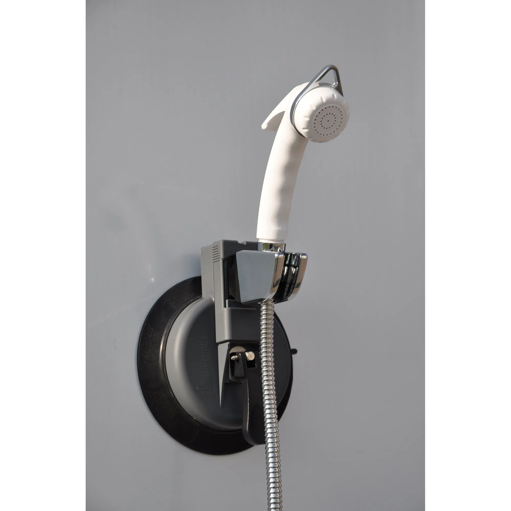Weißer Handbrausehalter mit runder schwarzer Saugnapfhalterung, verchromter Aufnahme und angeschlossenem Spiralschlauch an einer grauen Wand