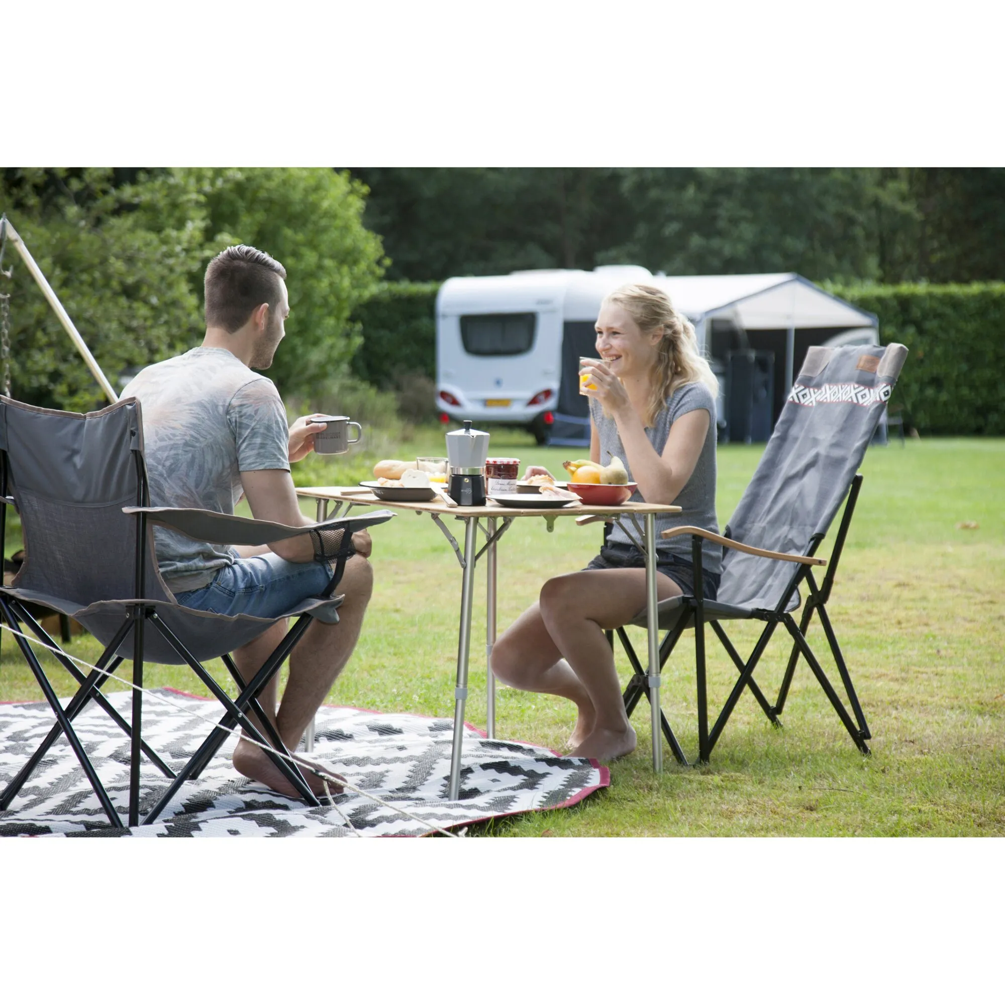 Campingtisch Suffolk mit silbernem Gestell und Holzoptik-Tischplatte, gedeckt mit Speisen und Getränken beim Camping genutzt