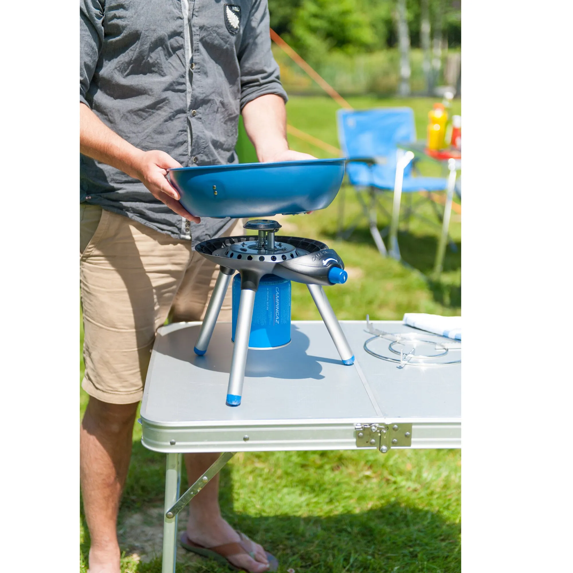 Person hält die blaue Grillschale des Party Grill 200 CV über dem aufgebauten Gasgrill mit Campingaz-Gaskartusche im Freien