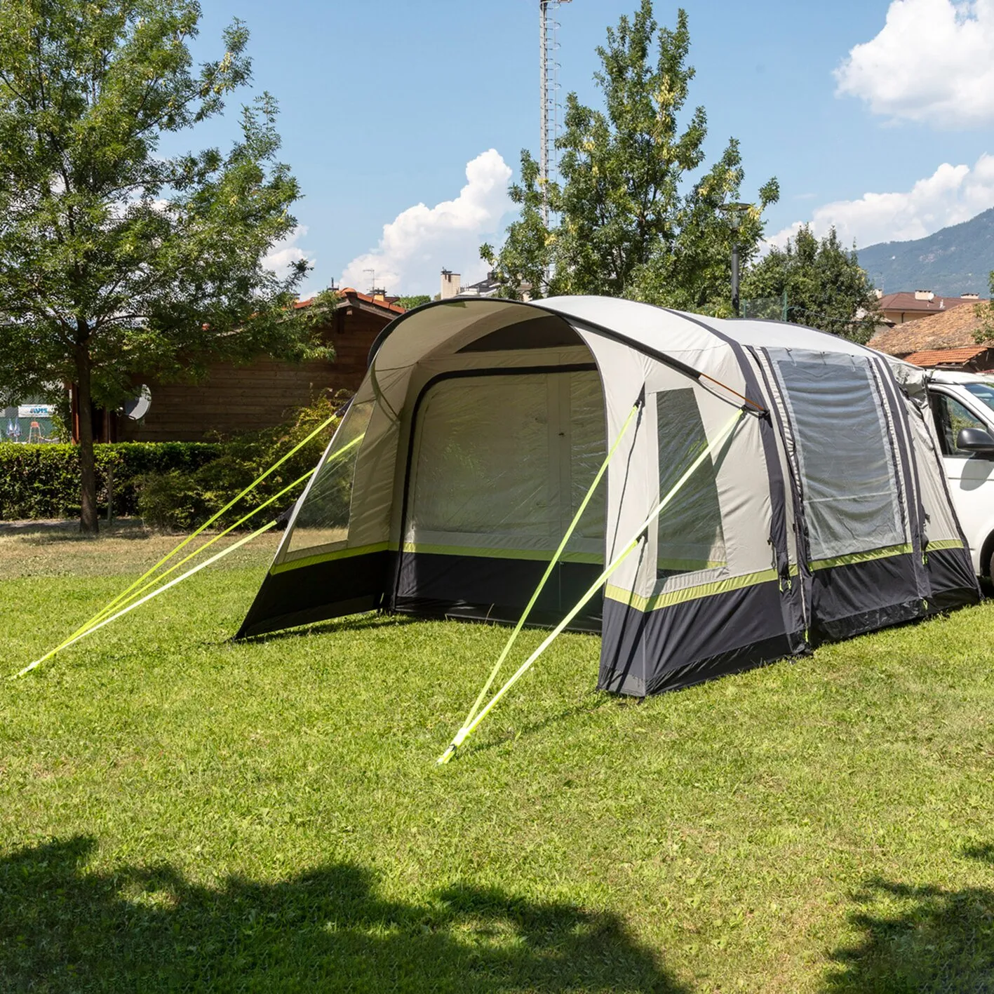 Busvorzelt Advantourer in Grau, Schwarz und Limettengrün, an einem weißen Campingbus befestigt und auf einer Wiese abgespannt