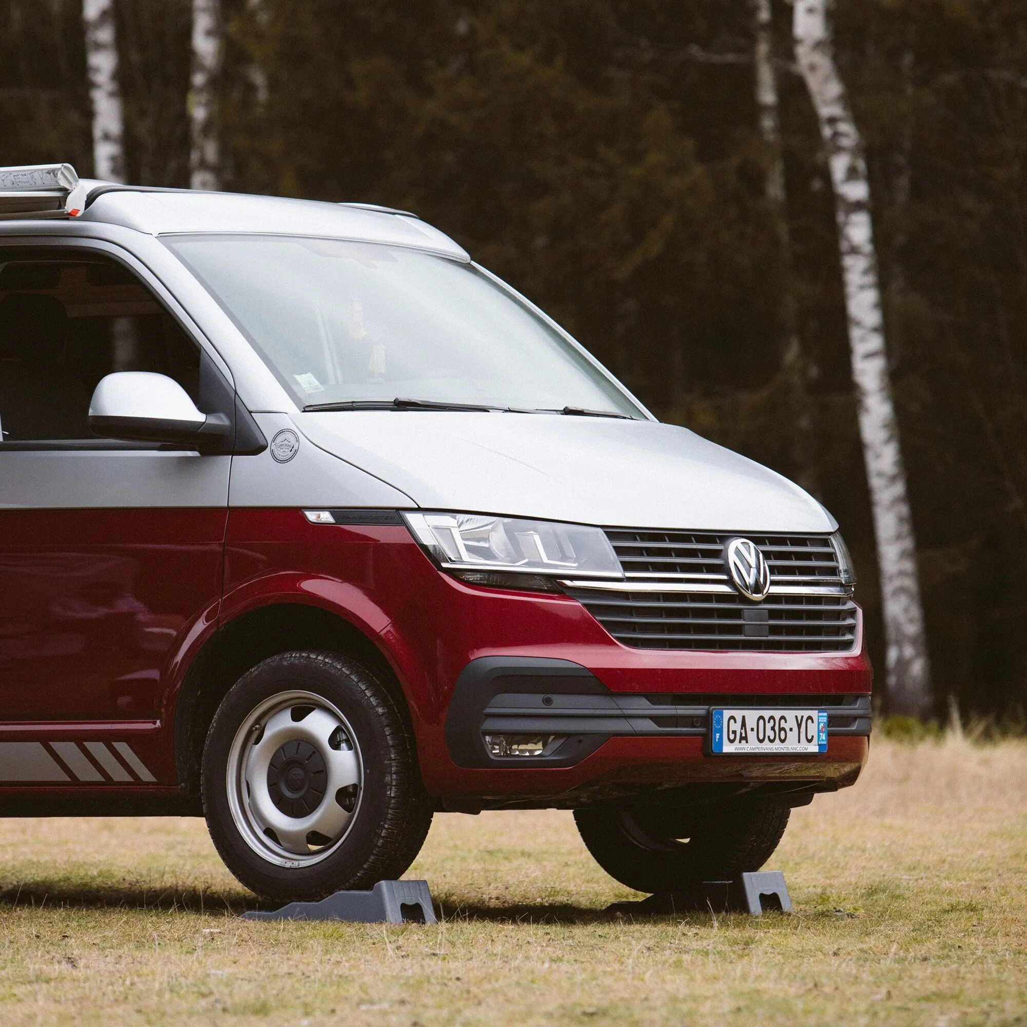 Roter Campingbus steht auf zwei grauen Auffahrkeilen des Level Up 2er-Sets auf einer Wiese im Wald